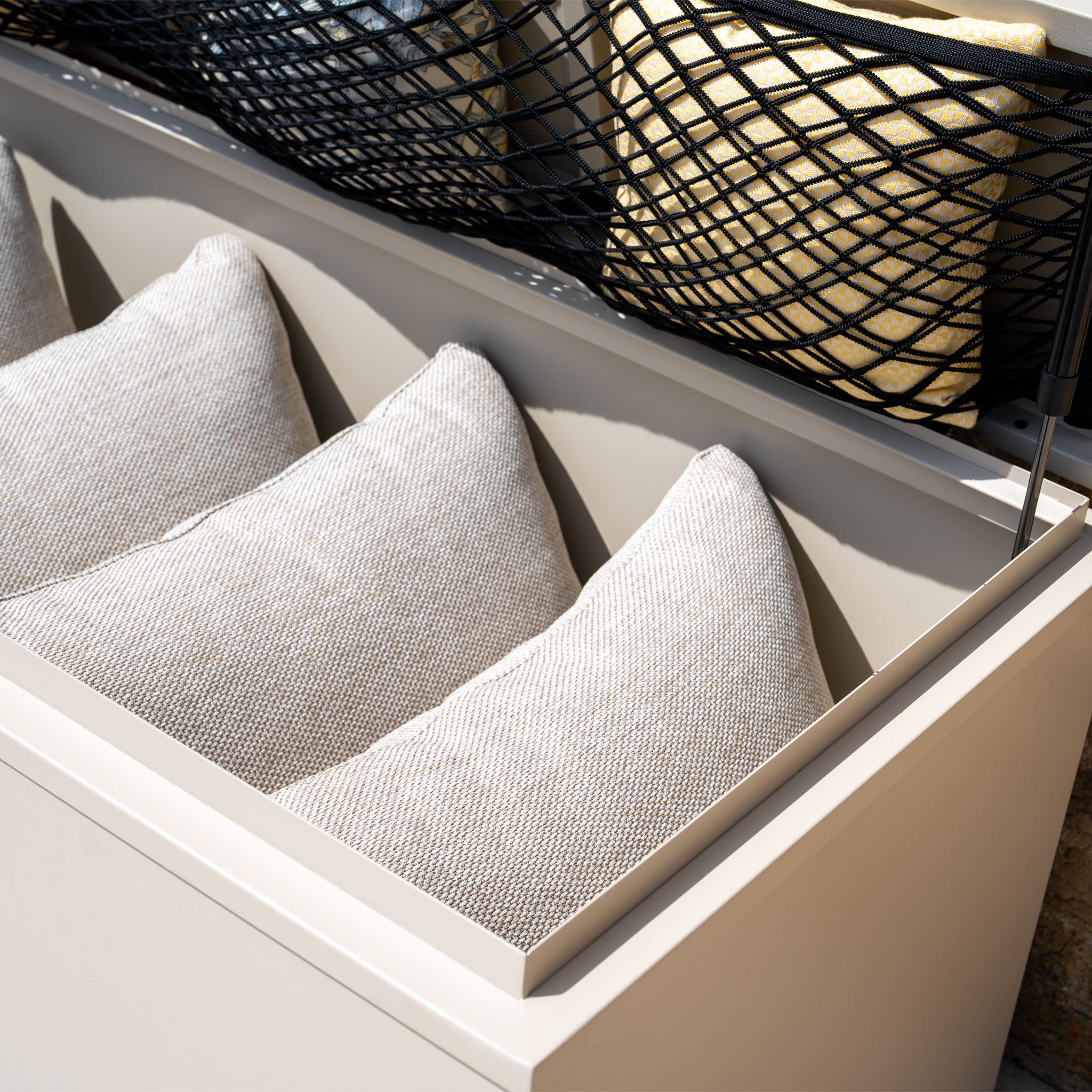 Three beige cushions neatly stored in a Large Steel Storage Box in Latte under a black net cover, perfect for outdoor storage.