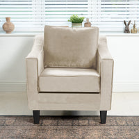 The Wiltshire Velvet Armchair in Cream takes center stage in the living room, with its soft texture enhanced by a rug and decorative window sill items. Handmade in England, this exquisite piece adds elegance to any space.