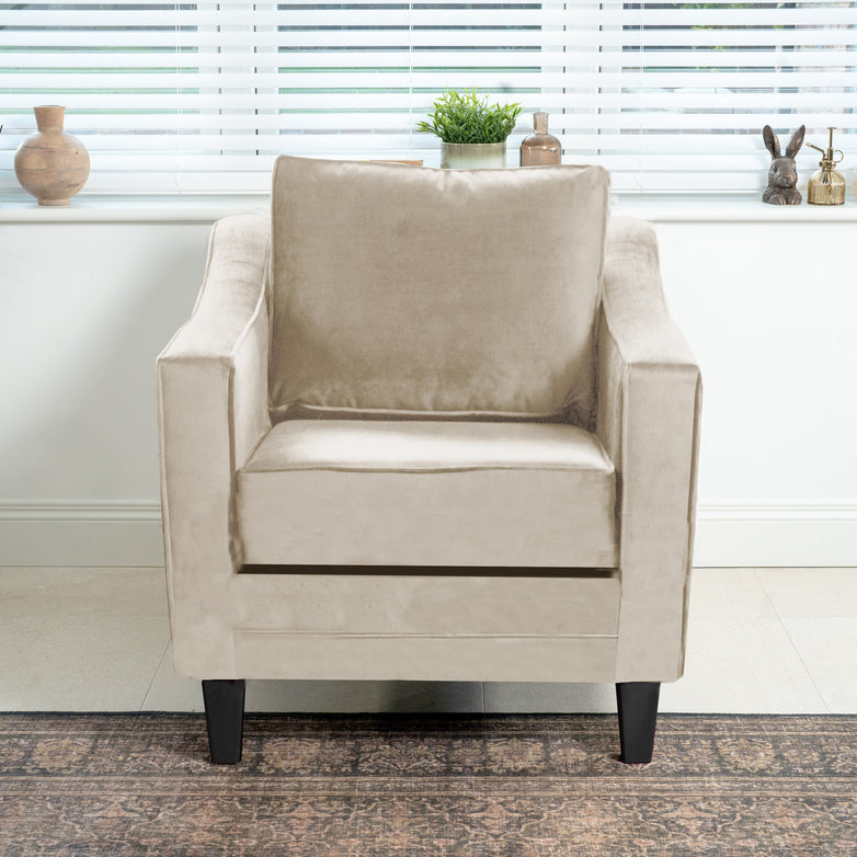 The Wiltshire Velvet Armchair in Cream takes center stage in the living room, with its soft texture enhanced by a rug and decorative window sill items. Handmade in England, this exquisite piece adds elegance to any space.