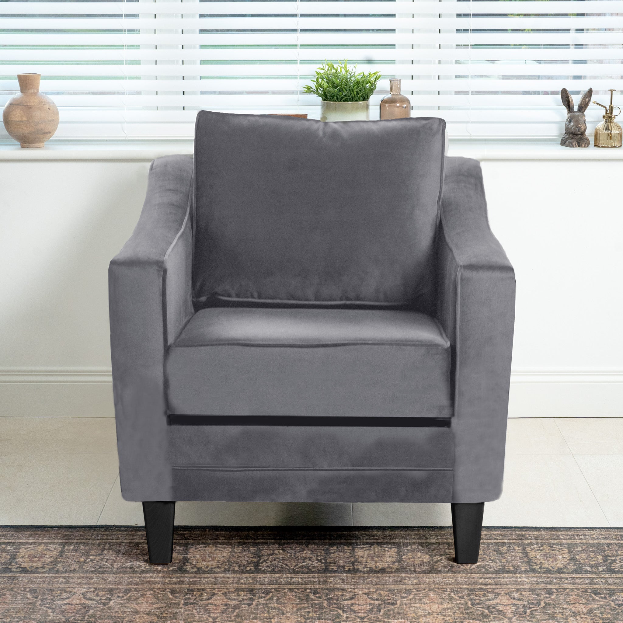 The Wiltshire Velvet Armchair in Steel Grey adds elegance with sustainable birch and beech wood. Stylish and eco-friendly, it fits perfectly in a room featuring a window, pottery, and a rug, making it an ideal addition to any contemporary living space.