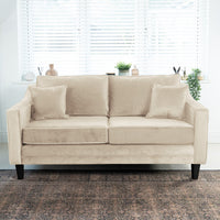 The Wiltshire 2 Seat Velvet Sofa in Cream, featuring two cushions, is placed before a window with white blinds and potted plants.