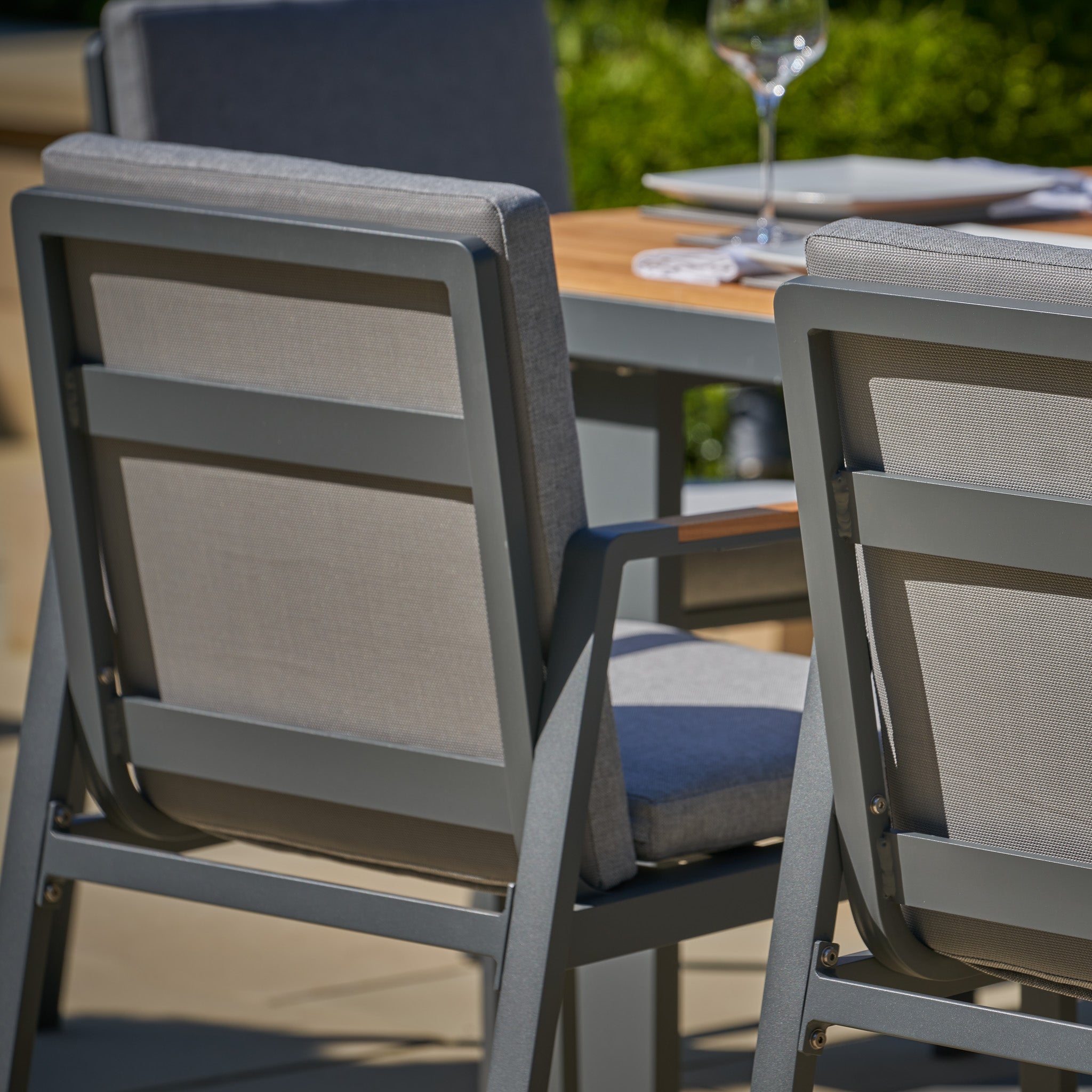 The Pacific Lifestyle - Stockholm 6 Seat Rectangular Dining Set in Marl Grey awaits in a sunny garden, complete with wine glass and plate for an idyllic meal.