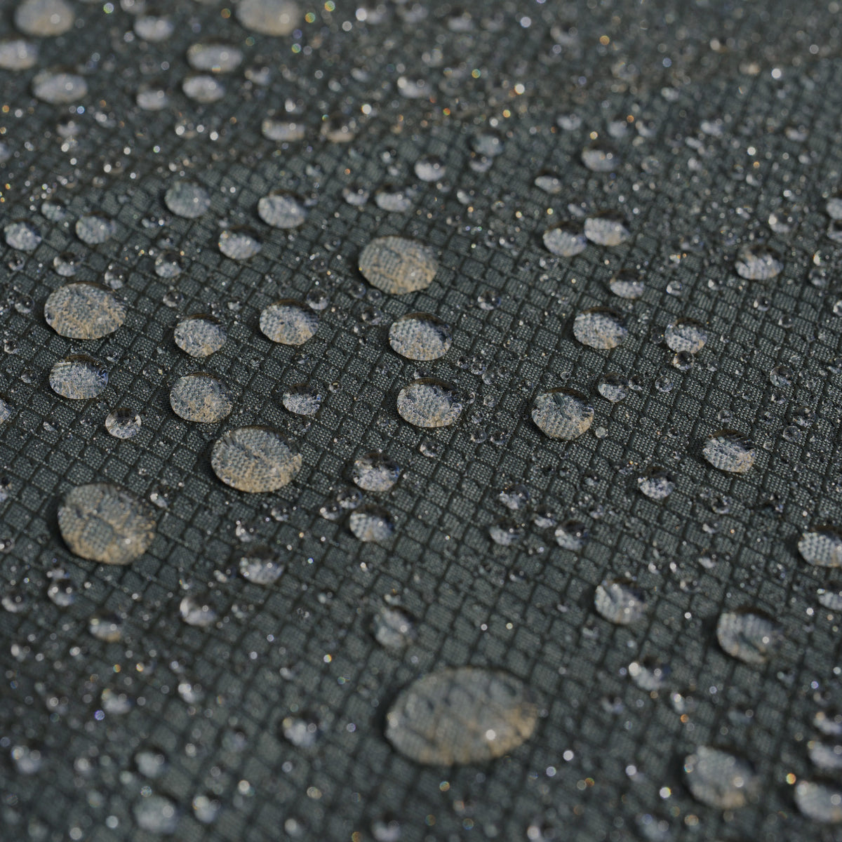 Water droplets scattered on a dark, textured, grid-patterned surface demonstrate the water resistance of the Stormtex Cushion Storage Bag 168 x 82 x 95cm.