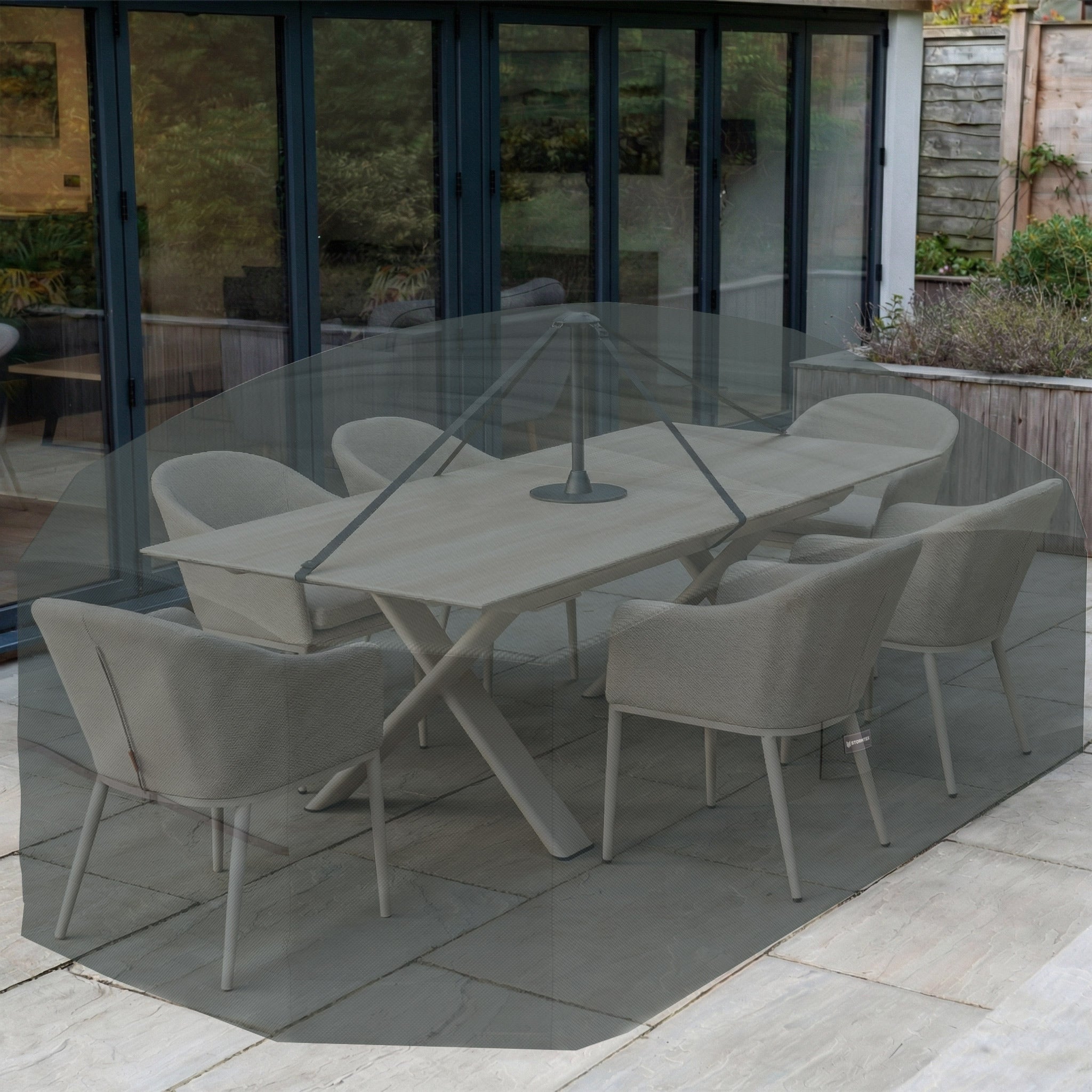 The Stormtex Water Shedding Pole supports a large patio umbrella over an outdoor dining set with six chairs, placed by glass doors and garden plants, offering enhanced protection for your garden furniture.