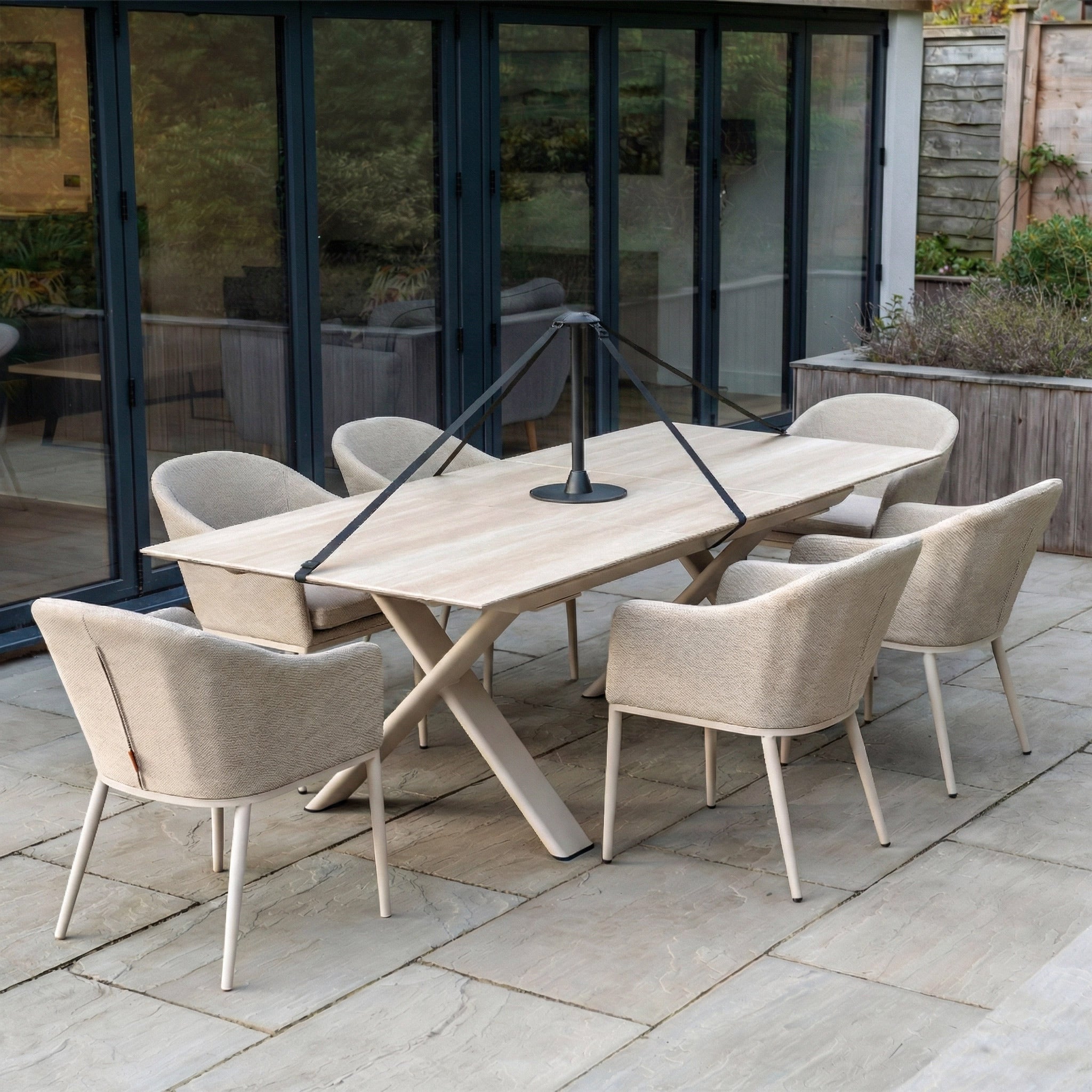 The Stormtex Water Shedding Pole provides added protection for your beige outdoor dining set with six chairs and a table, situated on a stone patio near glass doors, ensuring garden furniture stays dry and protected.