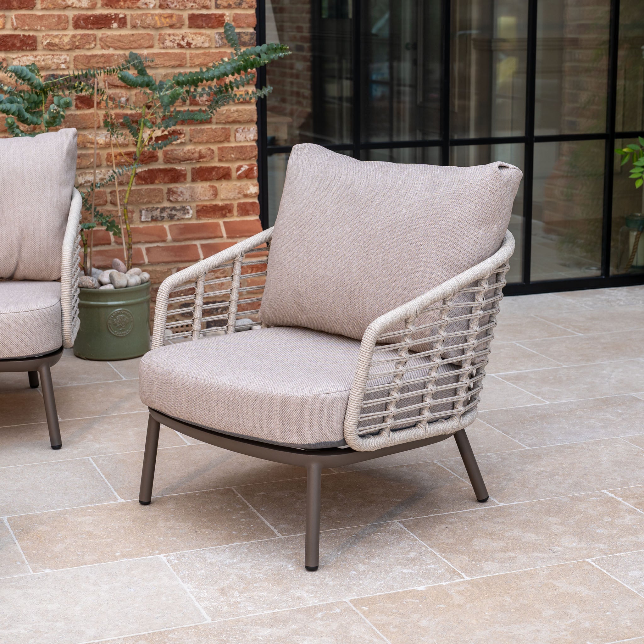 The Sutera 3 Seat Sofa Set in Putty features rope detailing and all-weather cushions, making it perfect garden furniture for a tiled patio near a brick wall and plants.