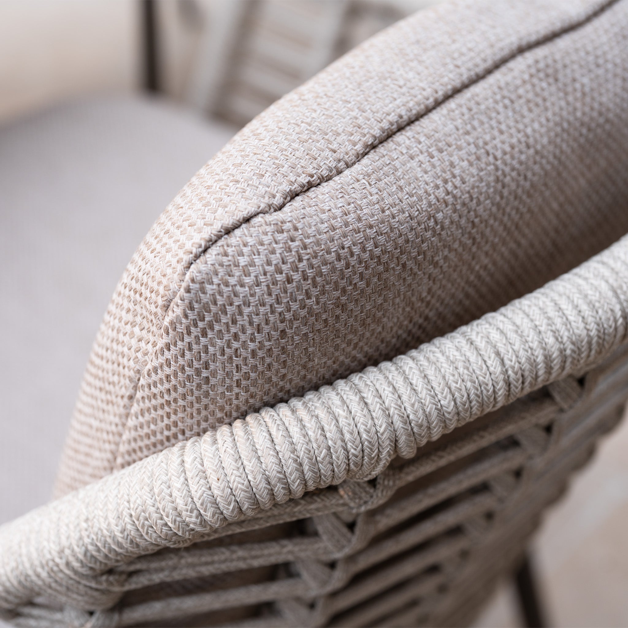 Close-up of the Sutera 6 Seat Curved Rectangular Dining Set in Putty, showing the beige woven chair’s detailed rope armrest and textured all-weather fabric cushion.