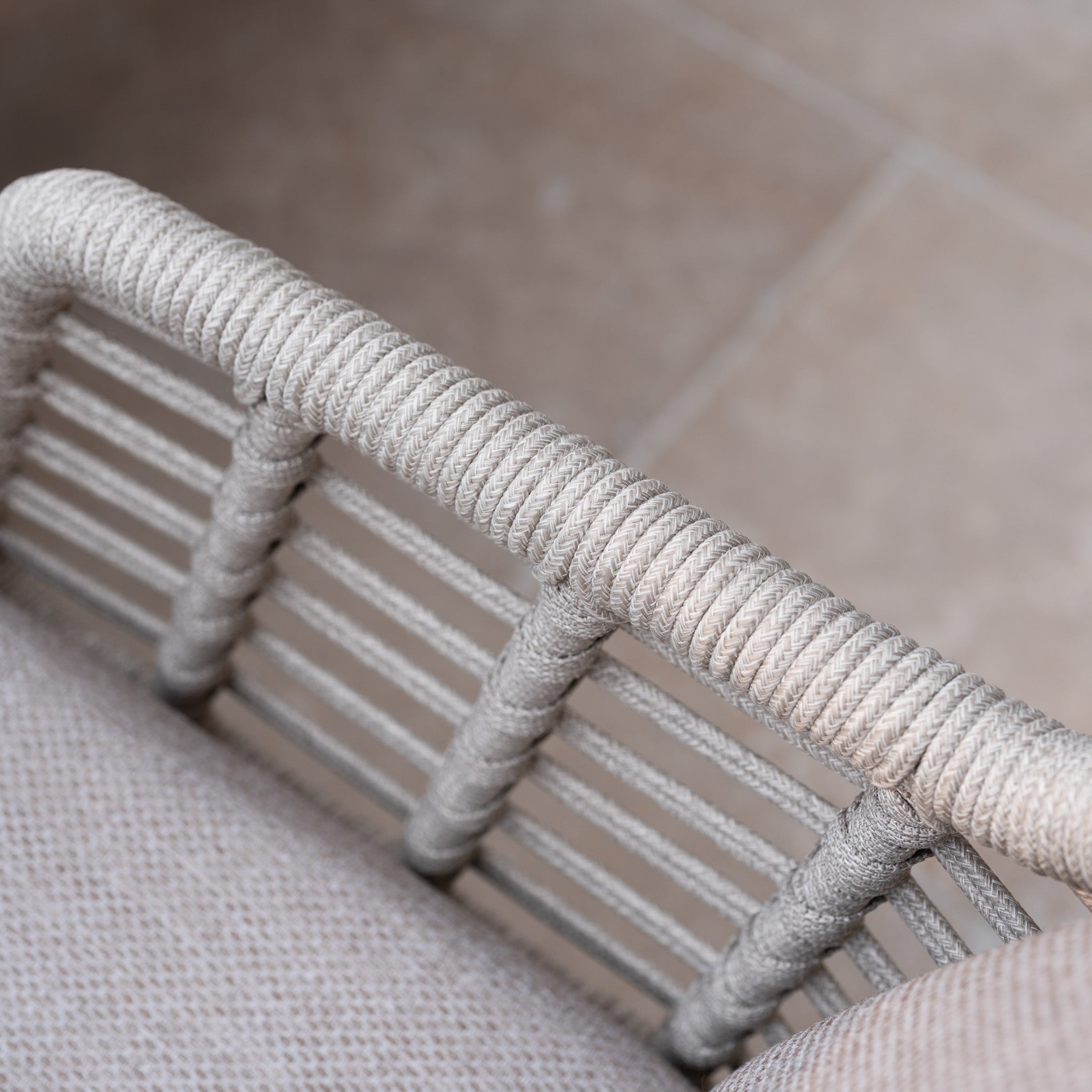 Close-up of a woven rope armrest on a light-colored chair from the Sutera 8 Seat Curved Rectangular Dining Set in Putty, shown with a tiled floor in the background as part of this elegant outdoor collection.