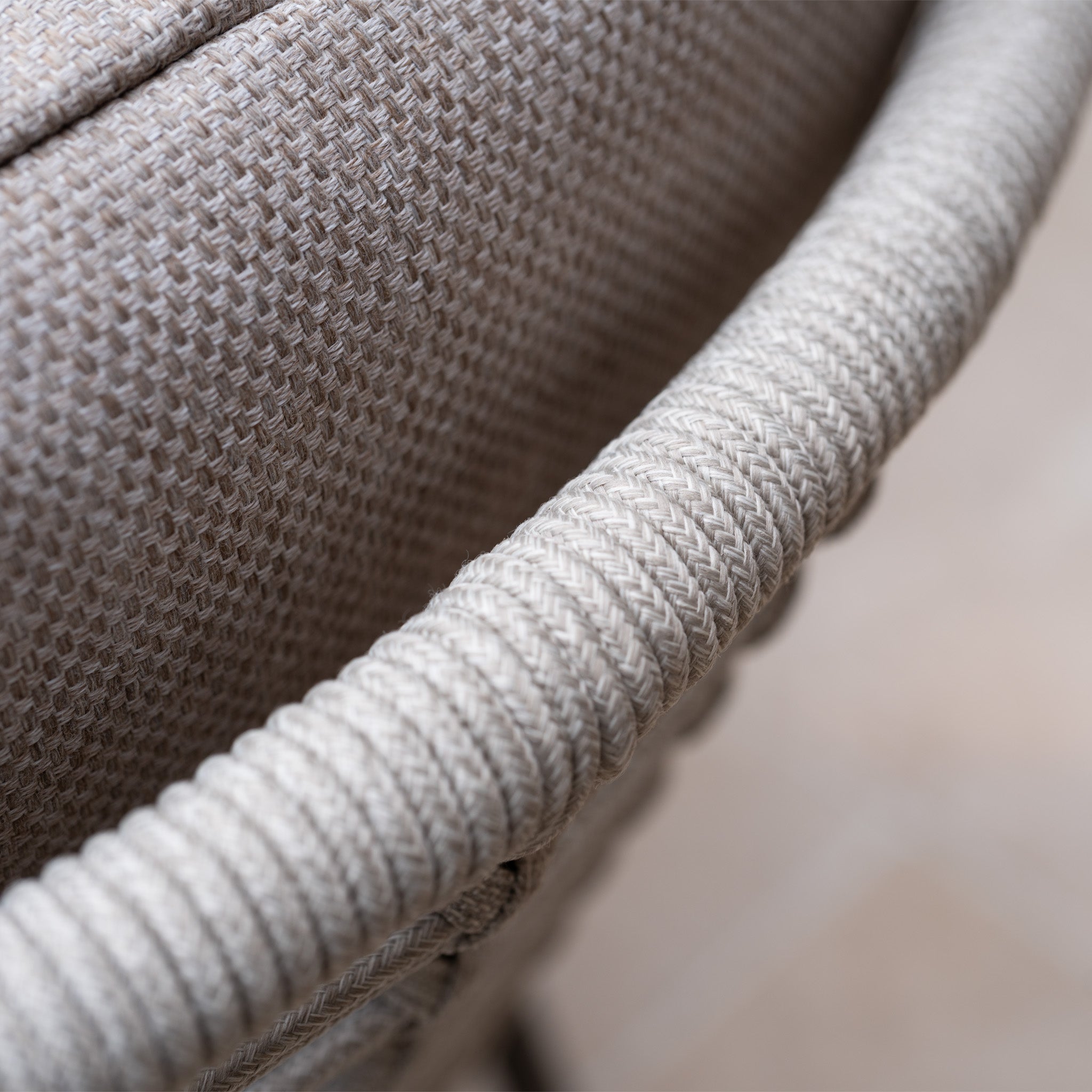 Close-up of the Sutera 8 Seat Curved Rectangular Dining Set in Putty, highlighting its woven beige chair with textured upholstery and a curved, braided armrest.