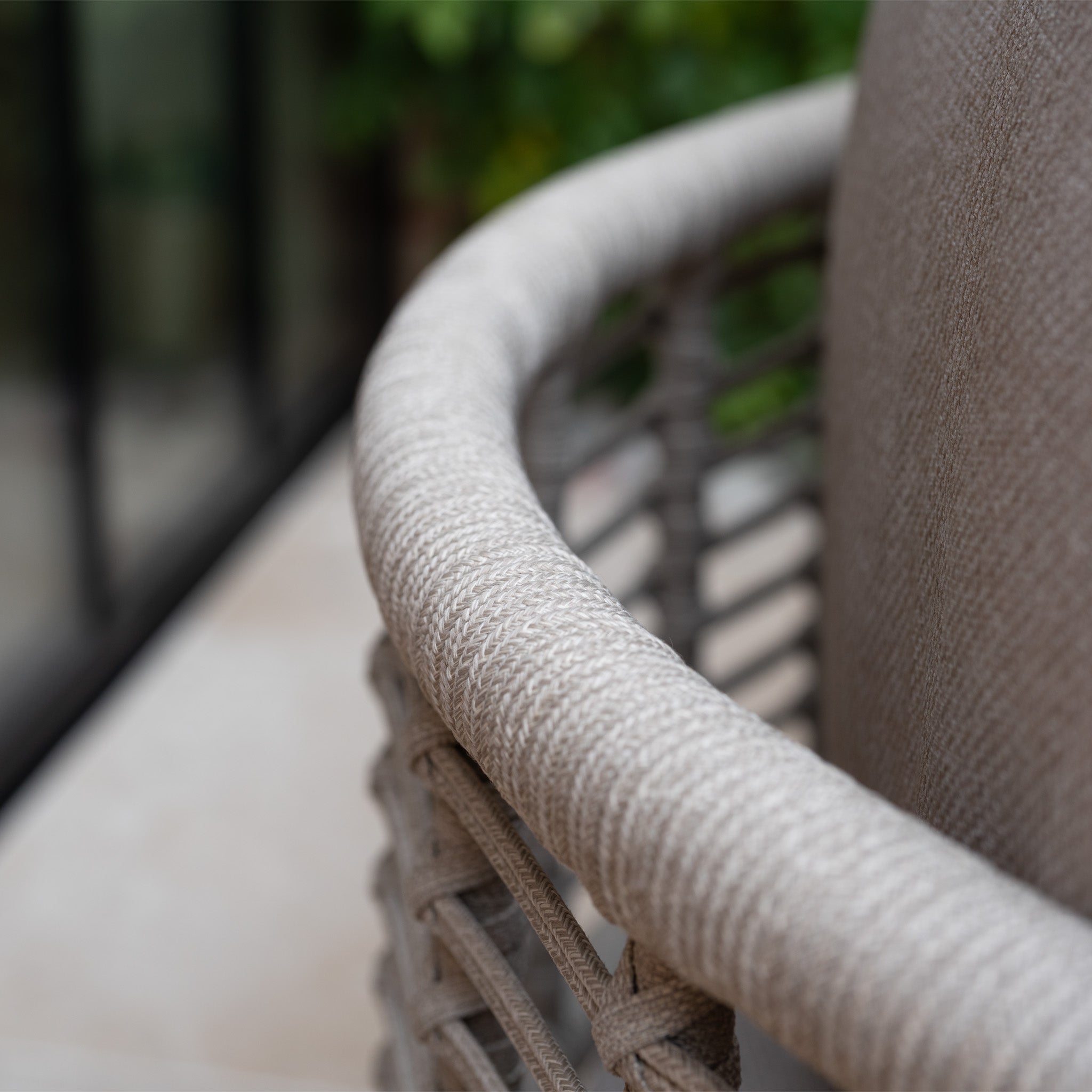 Close-up of a woven outdoor chair with curved armrest, cushioned backrest, and stylish rope design—perfectly complementing the Sutera Curved Chaise Sofa Set in Putty with all-weather cushions for lasting comfort.