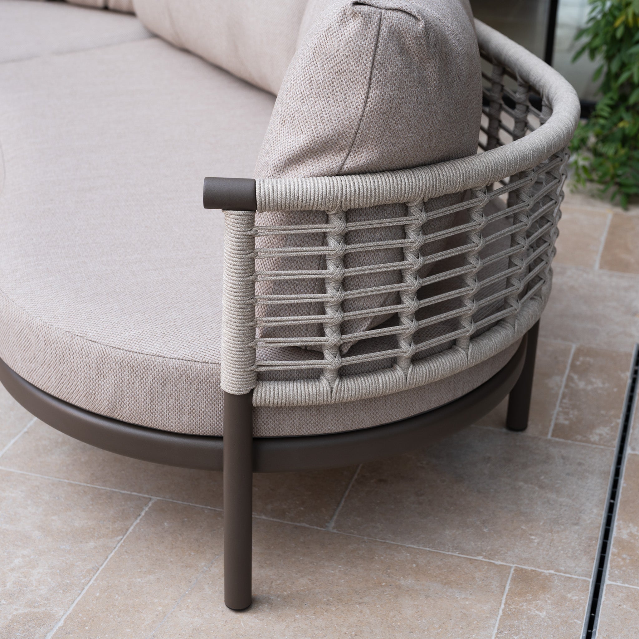 Close-up of the Sutera Curved Chaise Sofa Set in Putty with a woven rope backrest and all-weather cushions on a tiled patio.