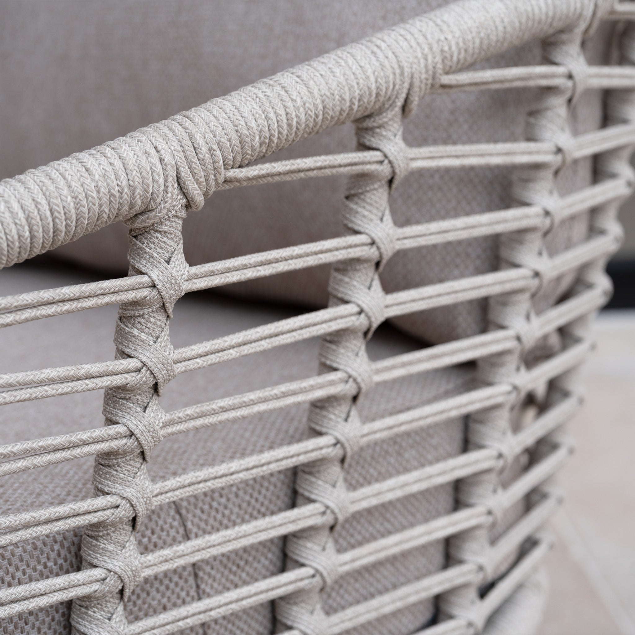 Close-up of woven rope wrapped around the armrest and frame of a modern outdoor chair with all-weather cushions, part of the Sutera Curved Chaise Sofa Set in Putty.