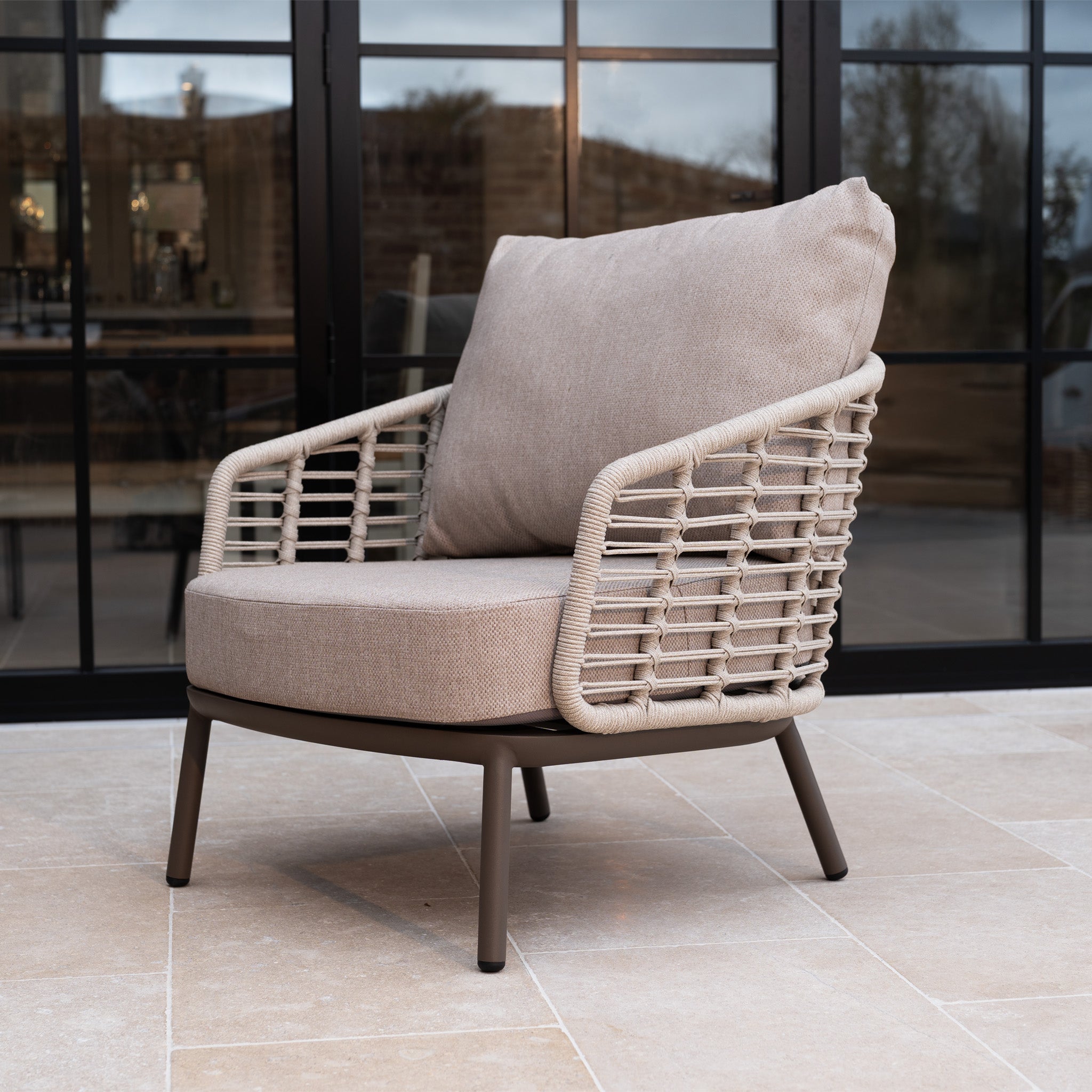 The Sutera Curved Chaise Sofa Set with Armchair in Putty features a beige outdoor lounge chair with all-weather cushions and woven sides—ideal stylish garden furniture for your patio.