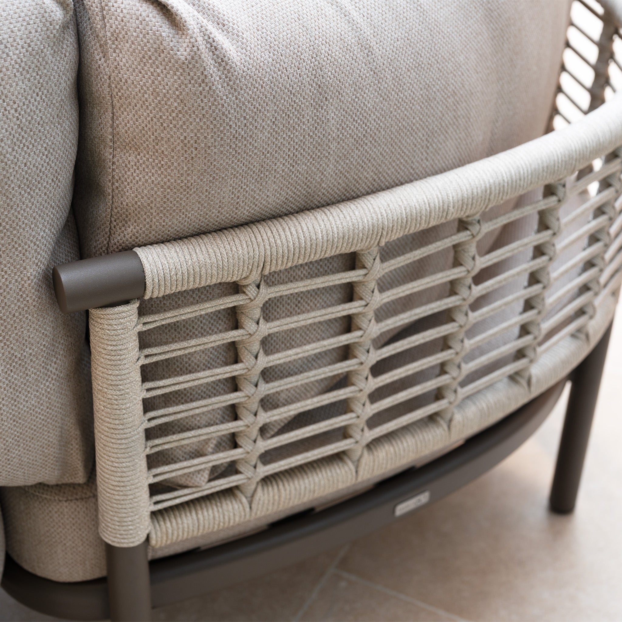 Close-up of a beige cushioned armchair with woven rope and metal backrest, part of the Sutera Curved Chaise Sofa Set with Armchair in Putty—stylish outdoor furniture featuring all-weather cushions.