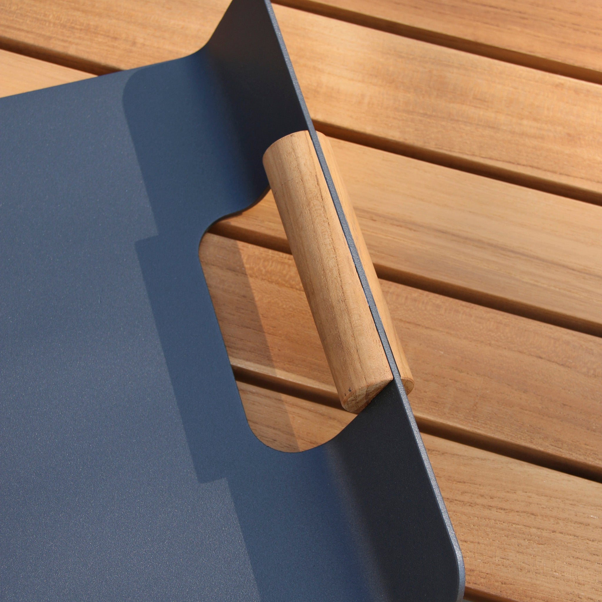 The FREE Tracy Serving Tray in charcoal, with teak handles, adds charm to any outdoor space as it rests gracefully on a light wooden surface—perfect for complementing garden furniture sets.