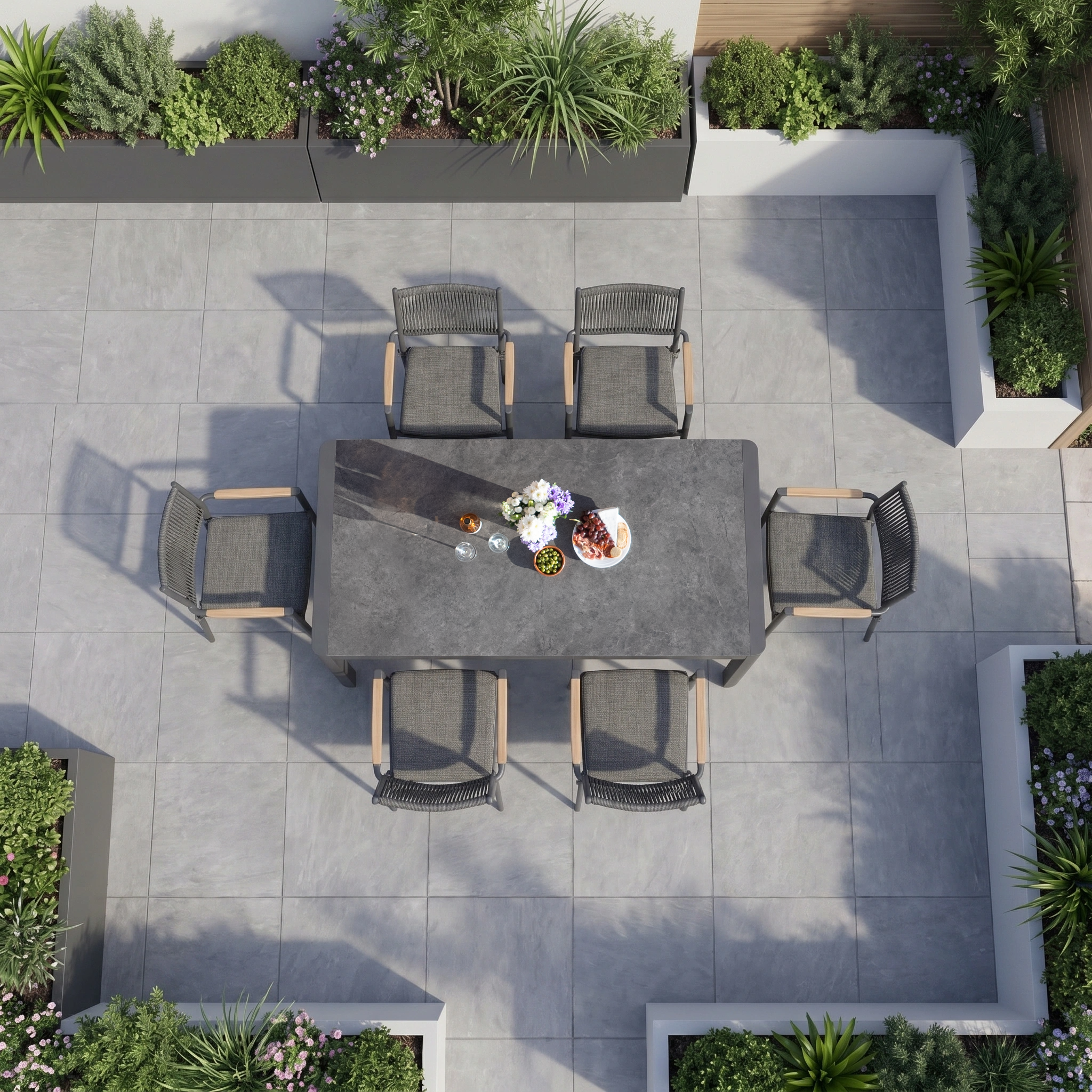The Tellaro 6 Seat Extending Dining Set in Grey, with a ceramic top table and six chairs, is surrounded by lush green plants and gray tile flooring in this overhead view.