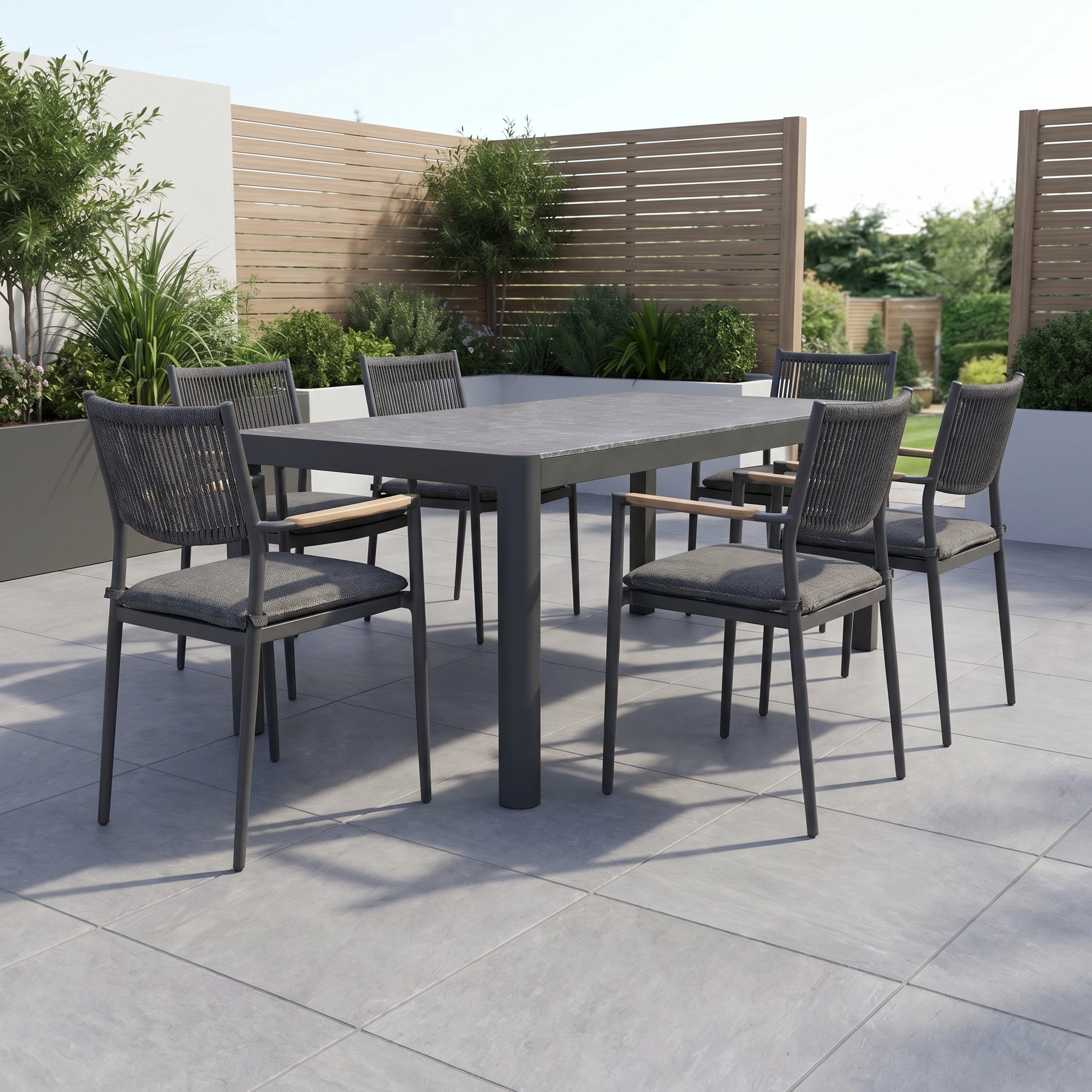 The Tellaro 6 Seat Extending Dining Set in Grey features a ceramic top table and six chairs, perfect for outdoor dining on a tiled patio with greenery and wooden privacy screens.