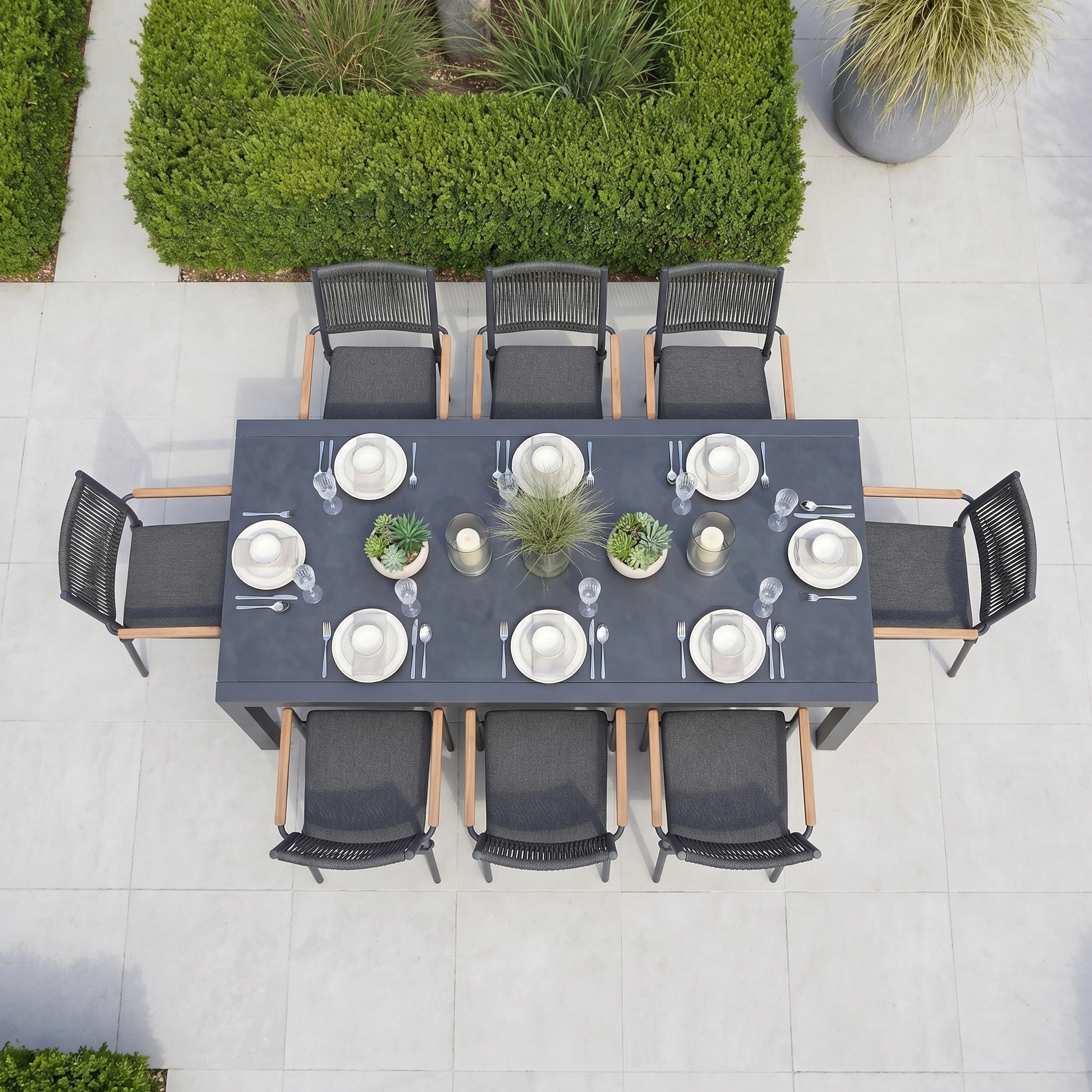 The Tellaro 8 Seat Extending Dining Set with Ceramic Table in Grey features a modern aluminium frame, dining essentials like plates and glasses, and is perfect for outdoor gatherings amid lush greenery.