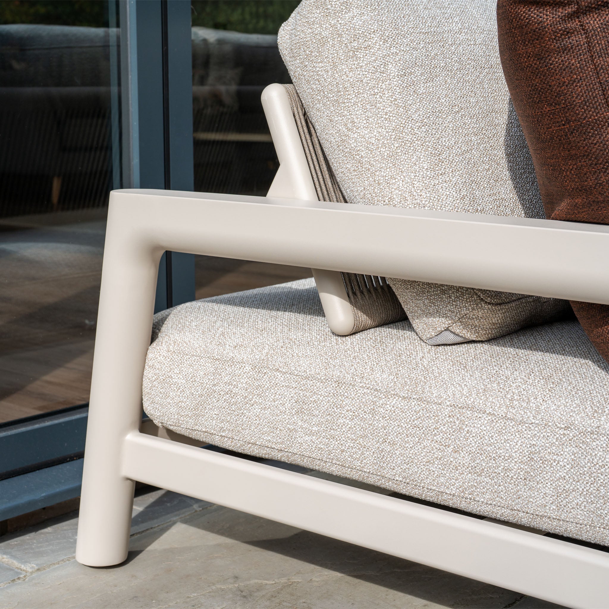 Close-up of the Theia 3 Seat Sofa Set in Oatmeal, featuring textured cushions and placed by a glass window—ideal for enhancing your modular garden furniture arrangement.