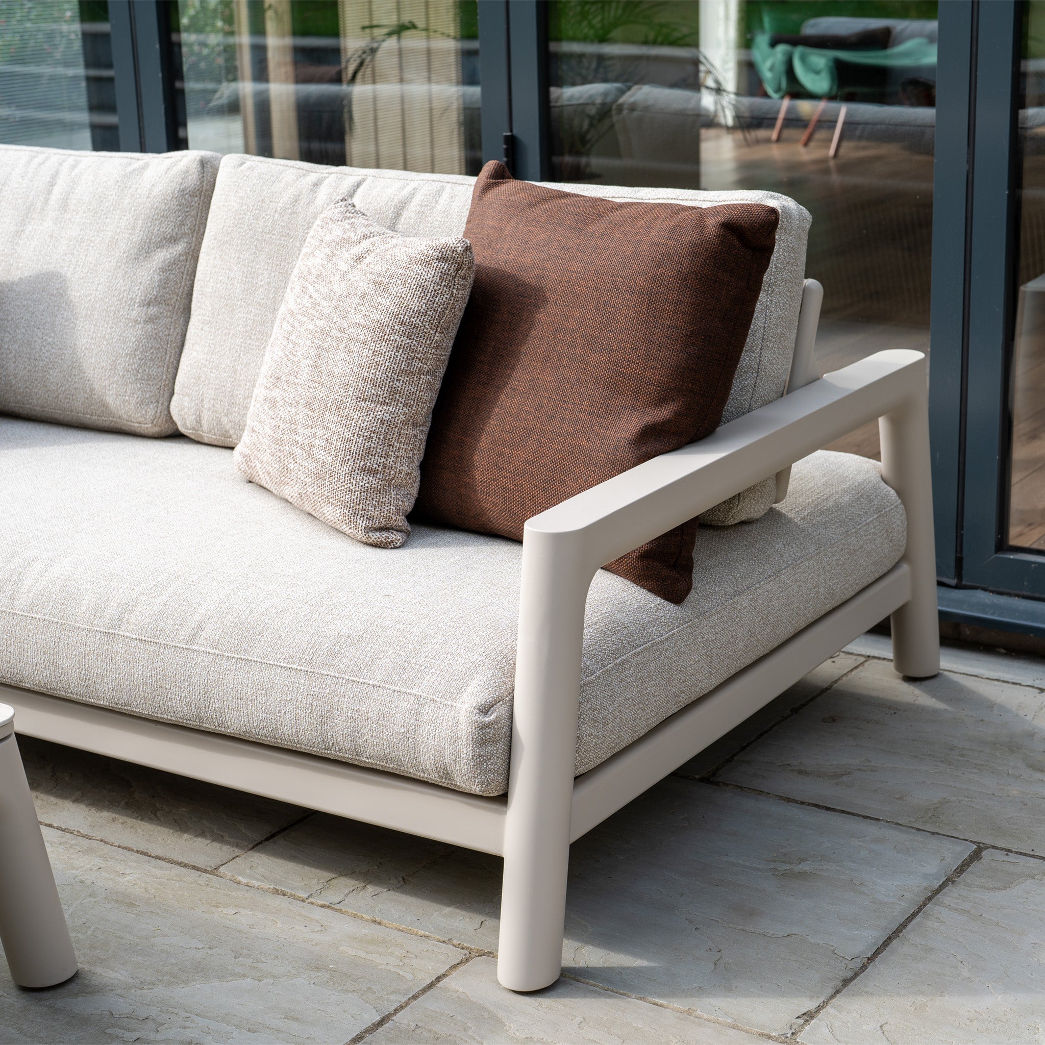 The Theia 3 Seat Sofa Set in Oatmeal with matching cushions is an ideal modular garden piece, perfect for relaxing on a stone patio beside large glass windows.