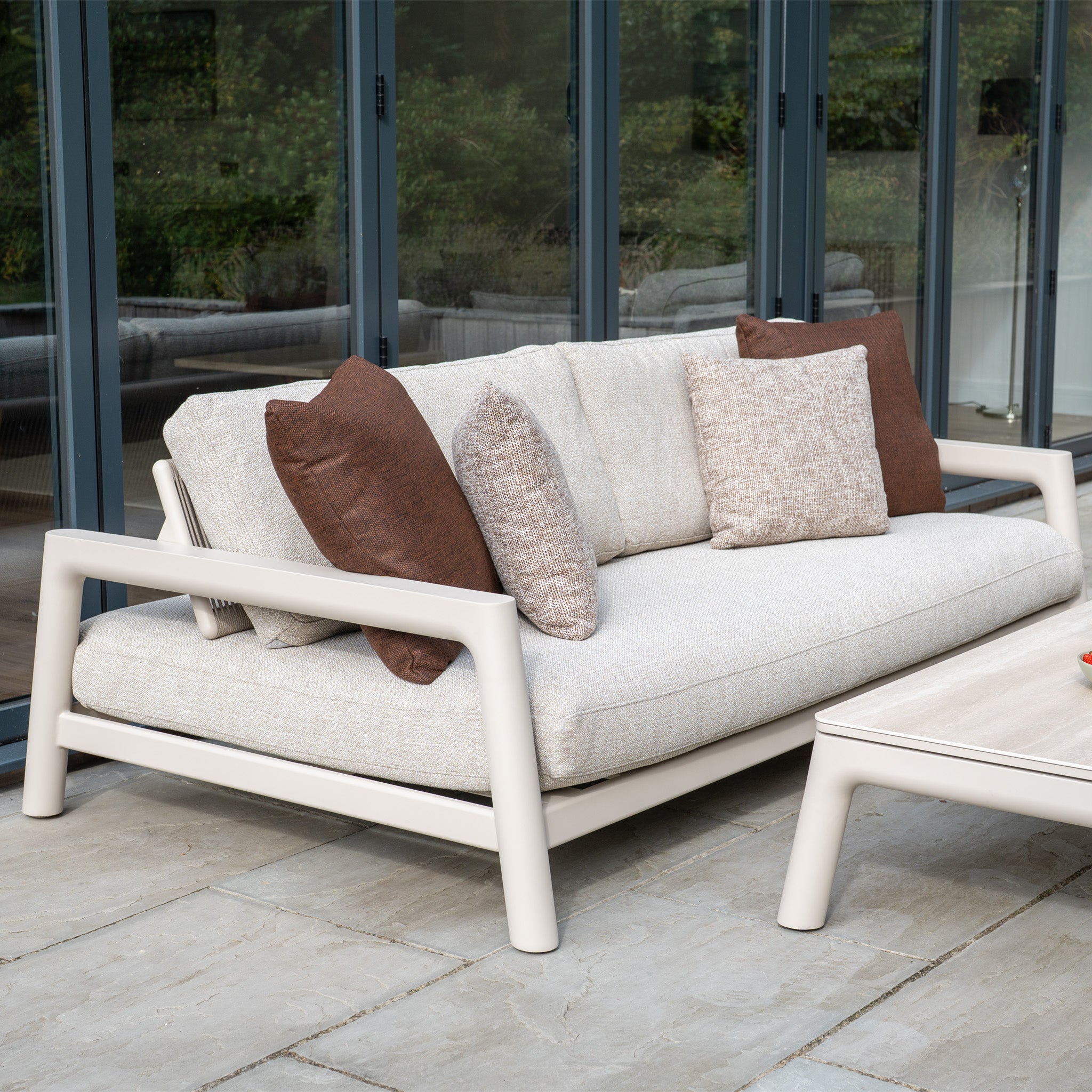 Theia 3 Seat Sofa Set in Oatmeal with brown and beige cushions is displayed on a stone patio beside glass doors.