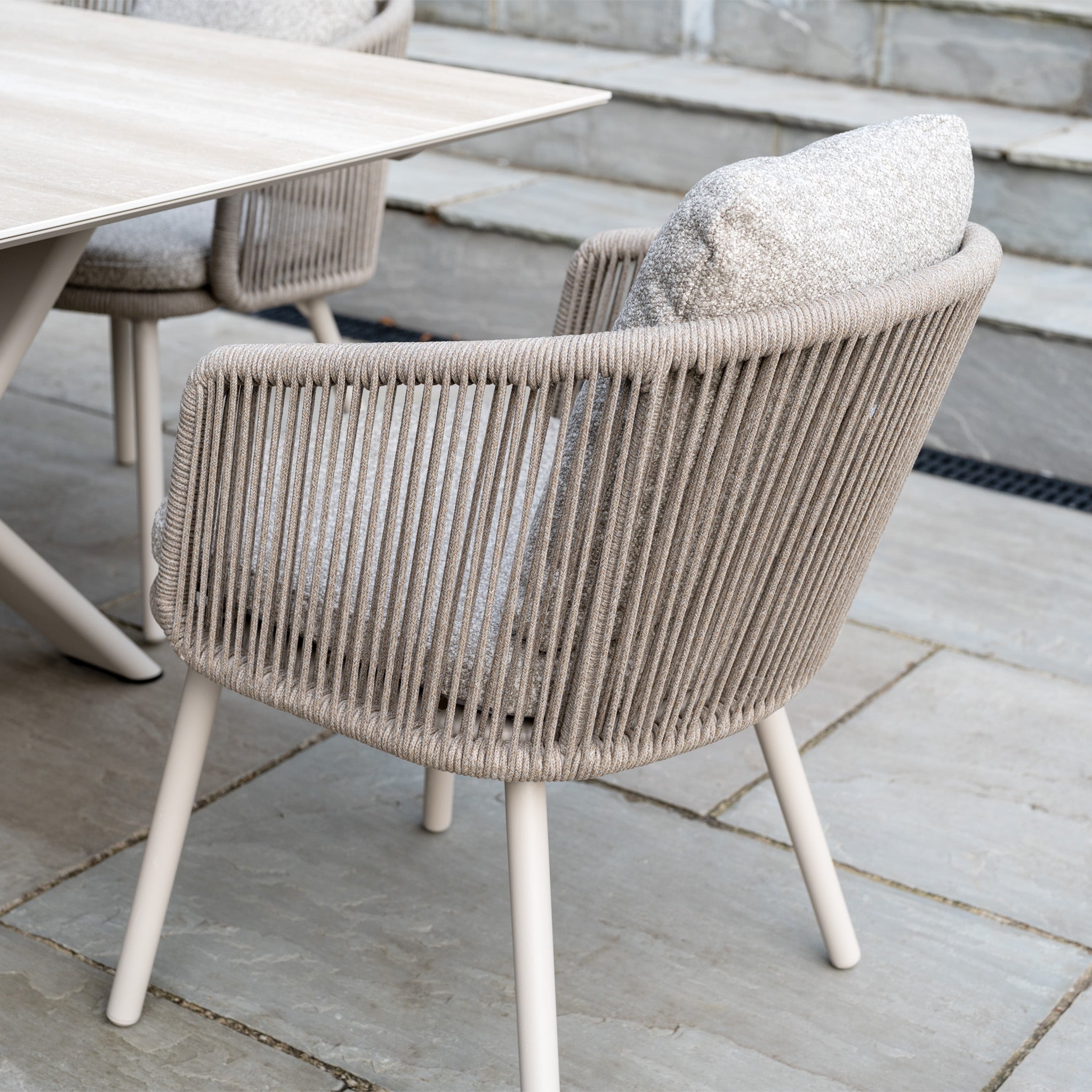 The Theia 6 Seat Rope Dining Set with Albatross Extending Table in Oatmeal is shown on a stone patio, perfect for elevating your outdoor dining experience.