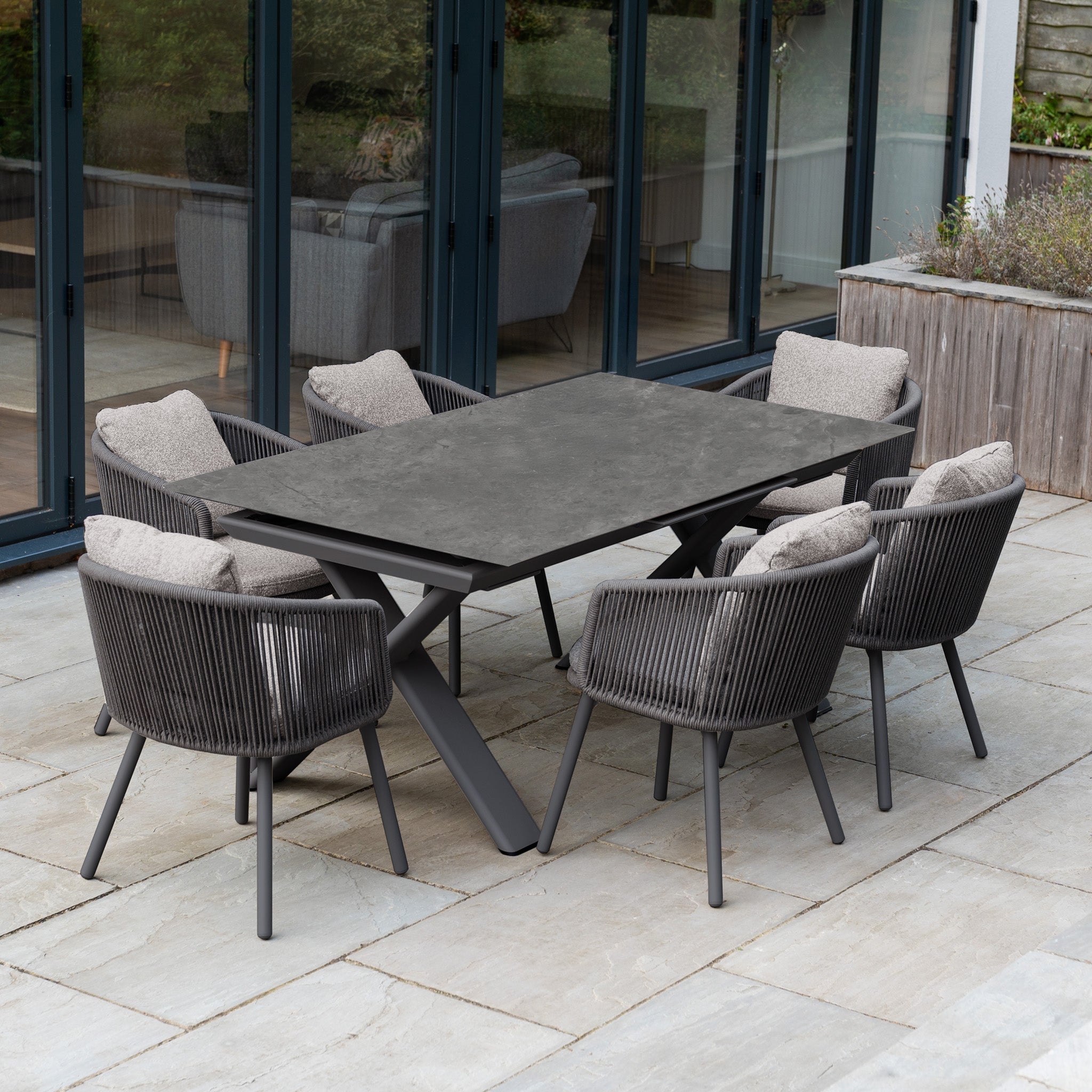 Theia 6 Seat Rope Dining Set with cushioned chairs and Albatross Extending Table in Truffle, arranged on a stone terrace for modern outdoor dining.