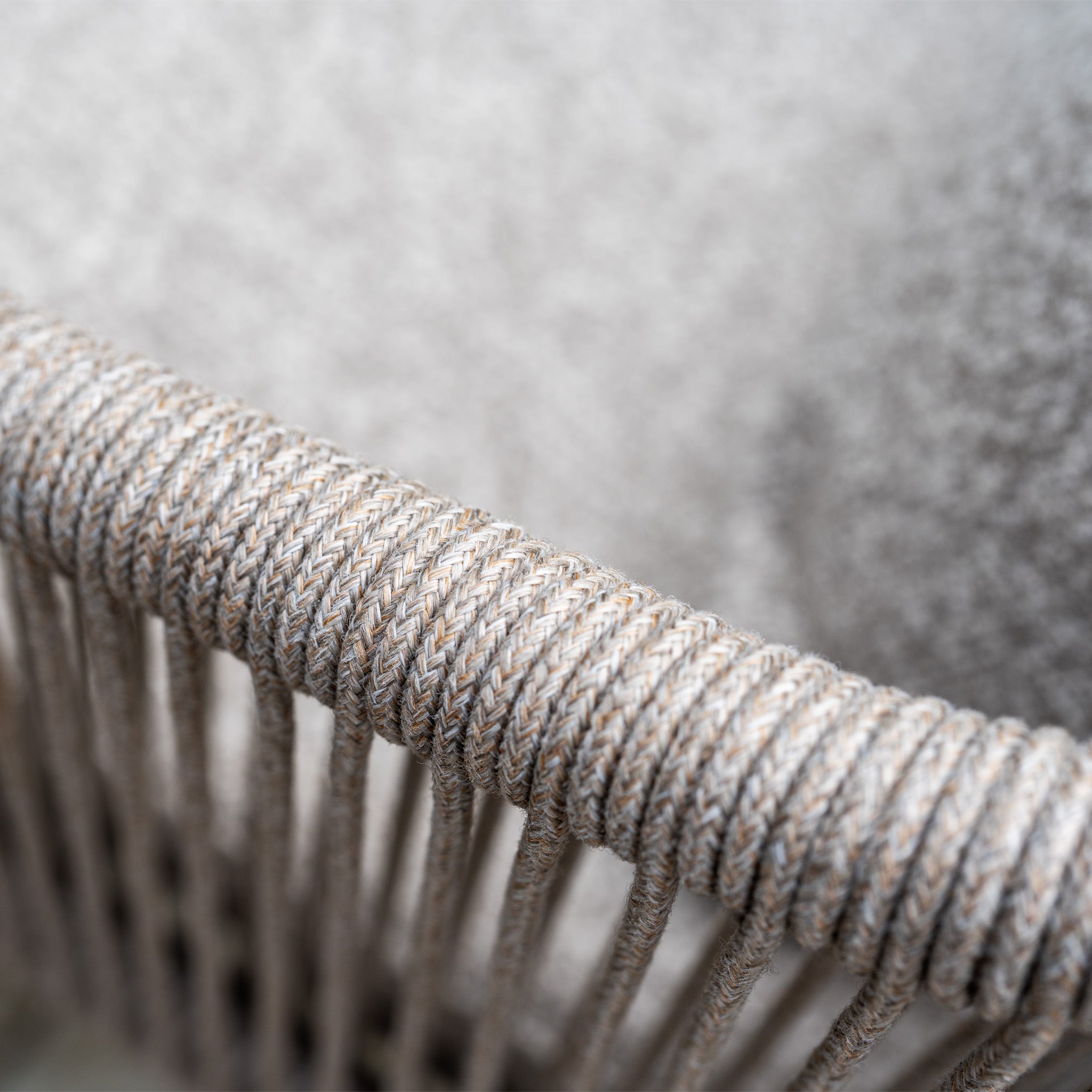 Close-up of beige rope woven around the curved frame of a chair from the Theia 8 Seat Rope Dining Set with Albatross Extending Table in Oatmeal, set against a soft textured background.