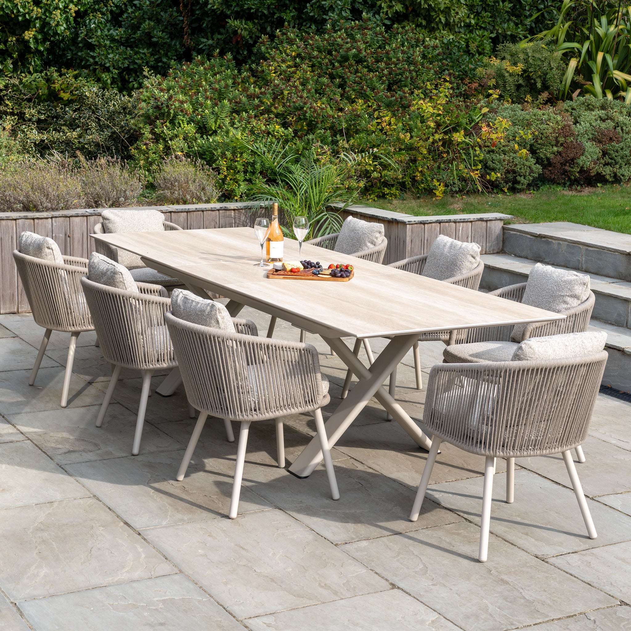 Theia 8 Seat Rope Dining Set with Albatross Extending Table in Oatmeal, arranged on a stone patio with cushioned chairs, drinks, and snacks for stylish outdoor dining.