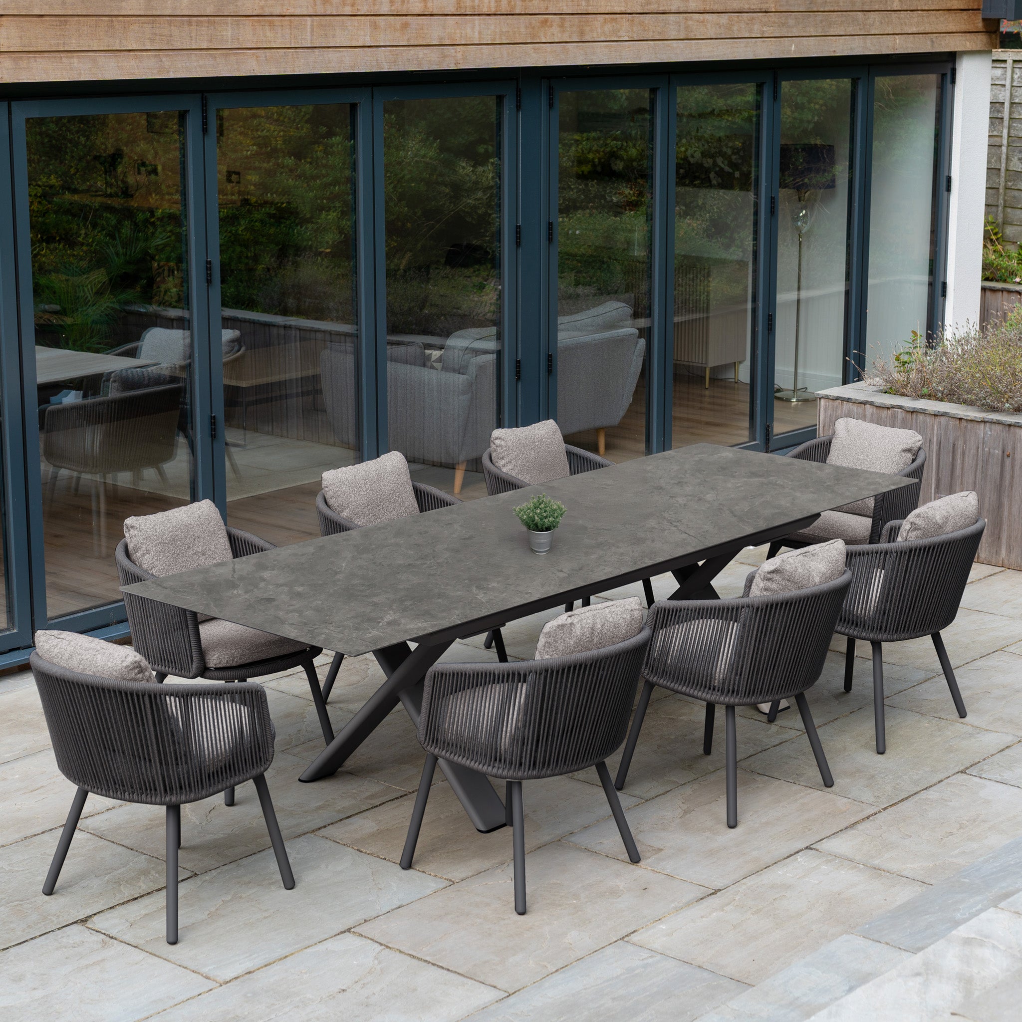 Experience stylish outdoor dining with the Theia 8 Seat Rope Dining Set, featuring cushioned chairs and the Albatross Extending Table in Truffle, perfect for your patio by the glass doors.