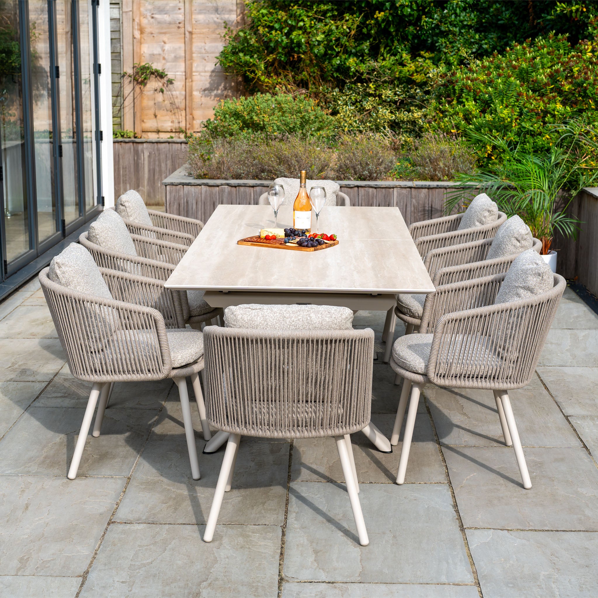 Theia 8 Seat Rope Dining Set with Albatross Extending Table in Oatmeal features eight cushioned rope chairs and a spacious table—ideal for stylish outdoor gatherings, easily holding wine and snacks for guests.