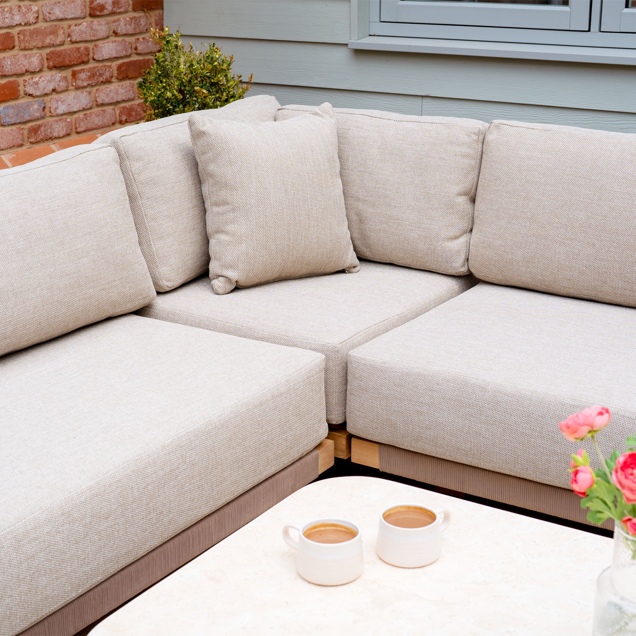 Tivoli Large Corner Set in Fawn with cushions and a marble coffee table, styled with two coffee mugs and pink flowers in the foreground.