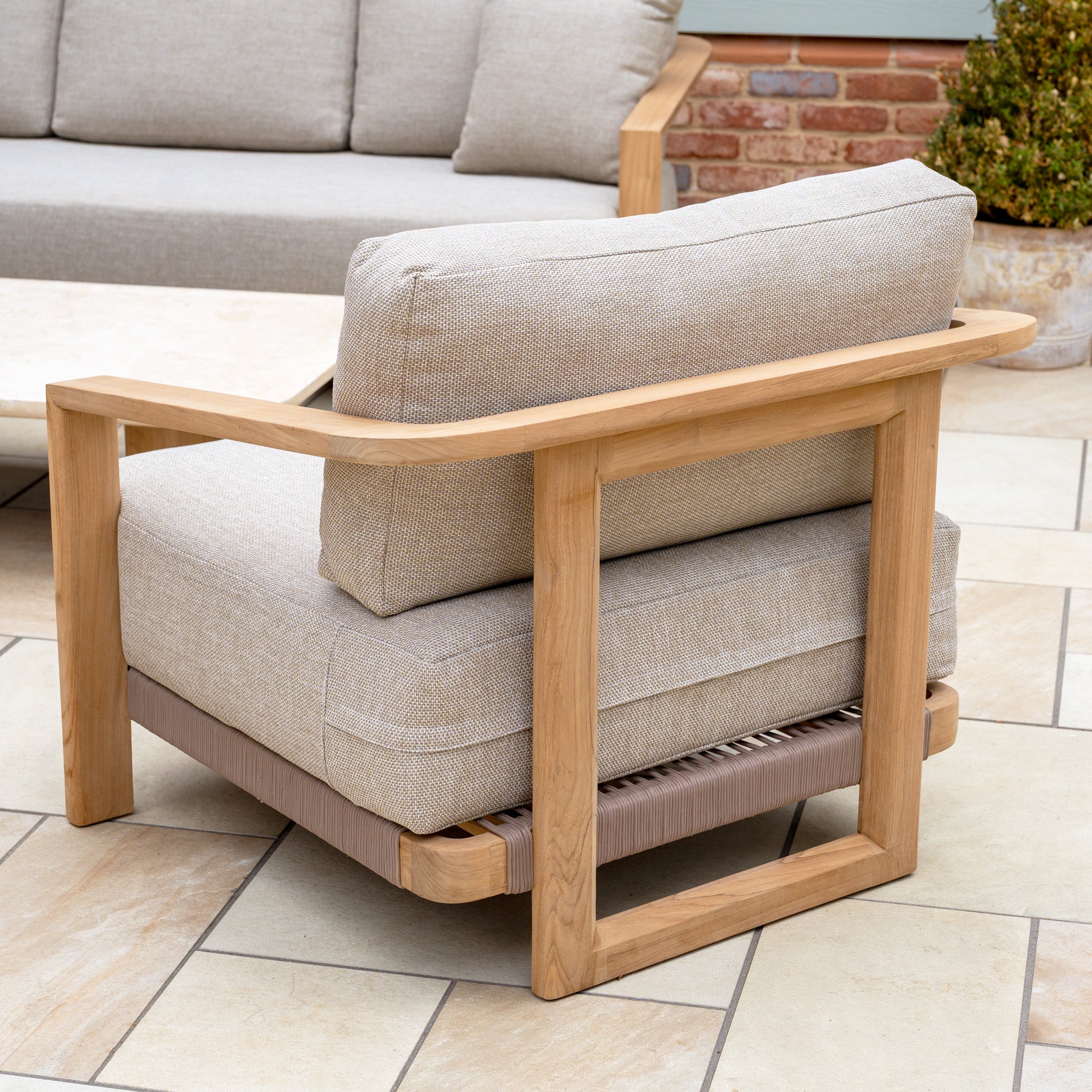 Modern outdoor armchair with teak wood frame and beige cushions on a tiled patio, perfectly complementing the Tivoli 3 Seat Sofa Set with Marble Coffee Table in Fawn.
