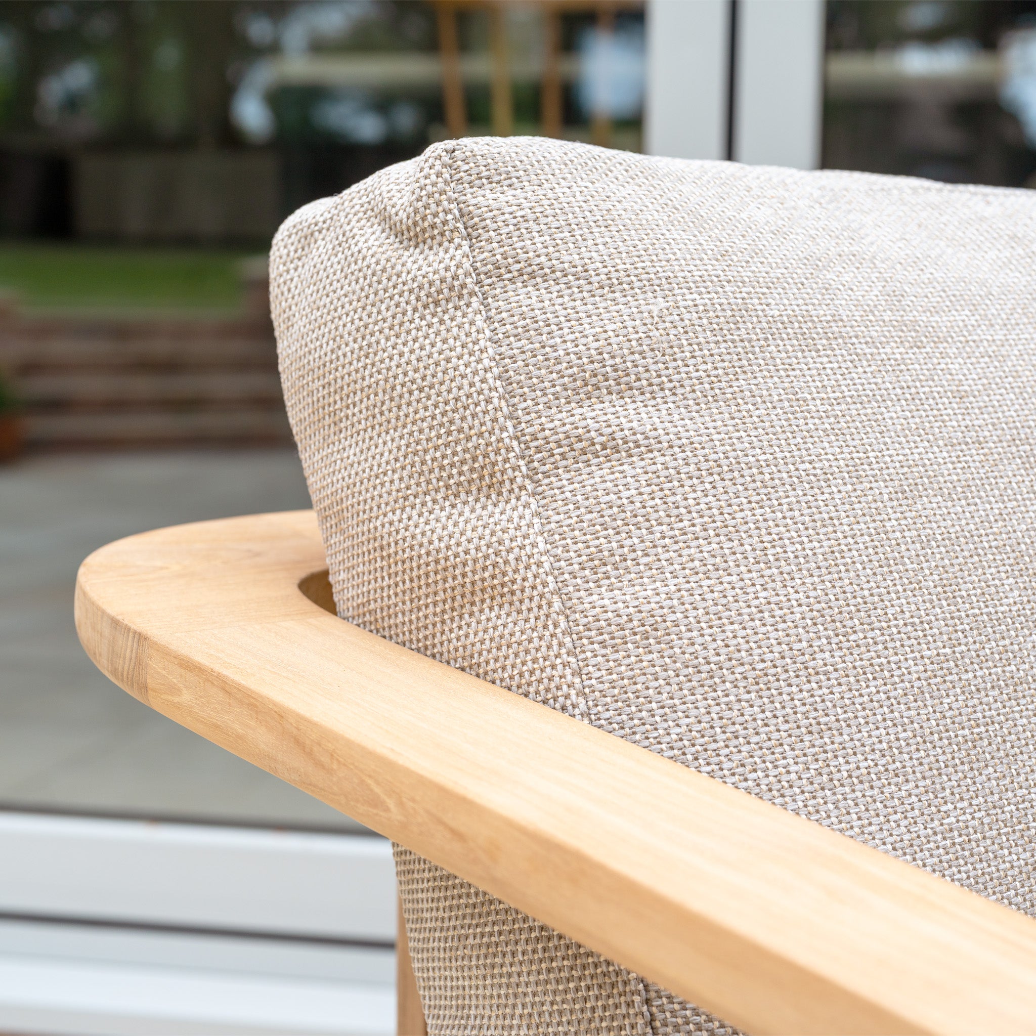 Close-up of the Tivoli 3 Seat Sofa Set with Marble Coffee Table in Fawn, featuring a beige textured cushion on a light teak wood armrest, placed outdoors near a window.