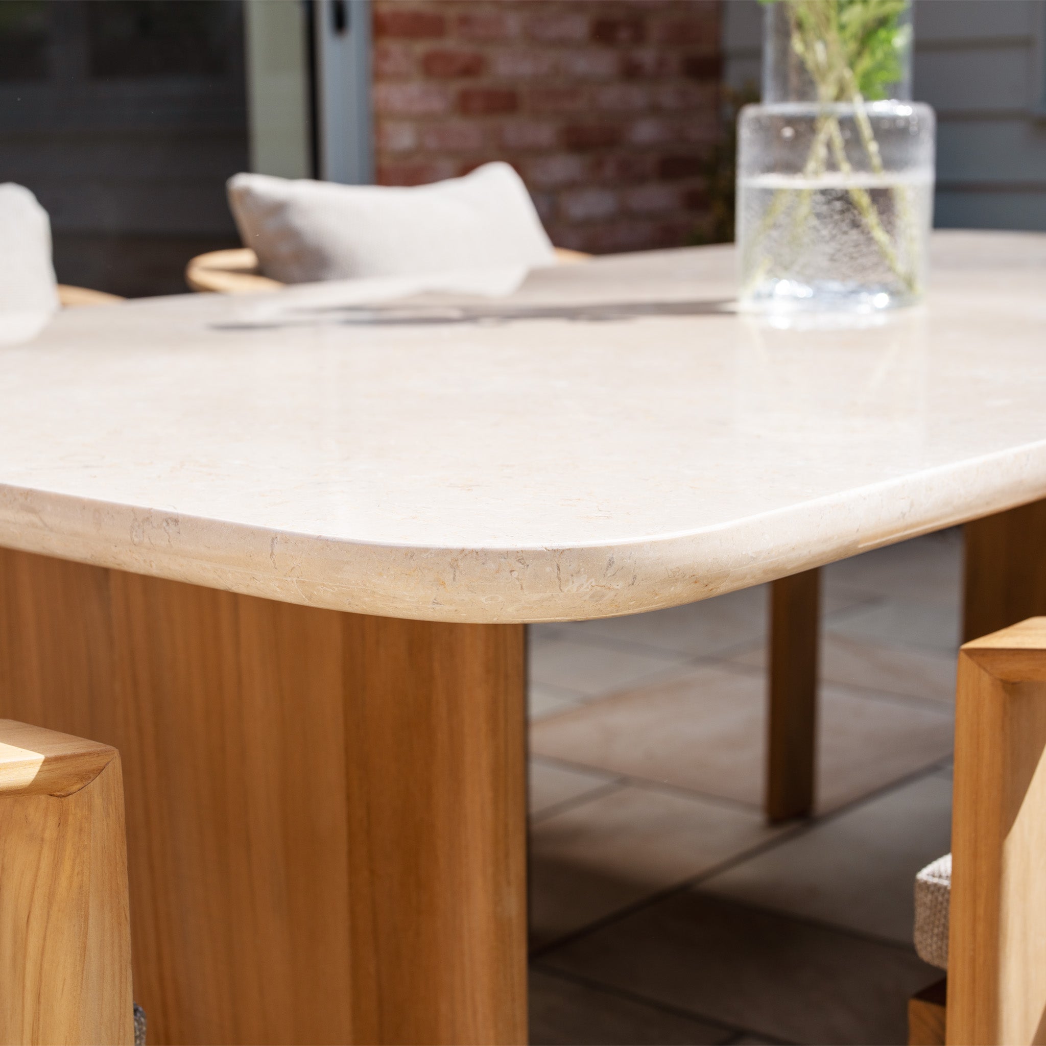 The Tivoli 6 Seat Dining Set with Marble Dining Table in Fawn includes a marble table and chairs, perfect for your patio, complete with cushions and stylish details like teak-look legs and a glass vase.