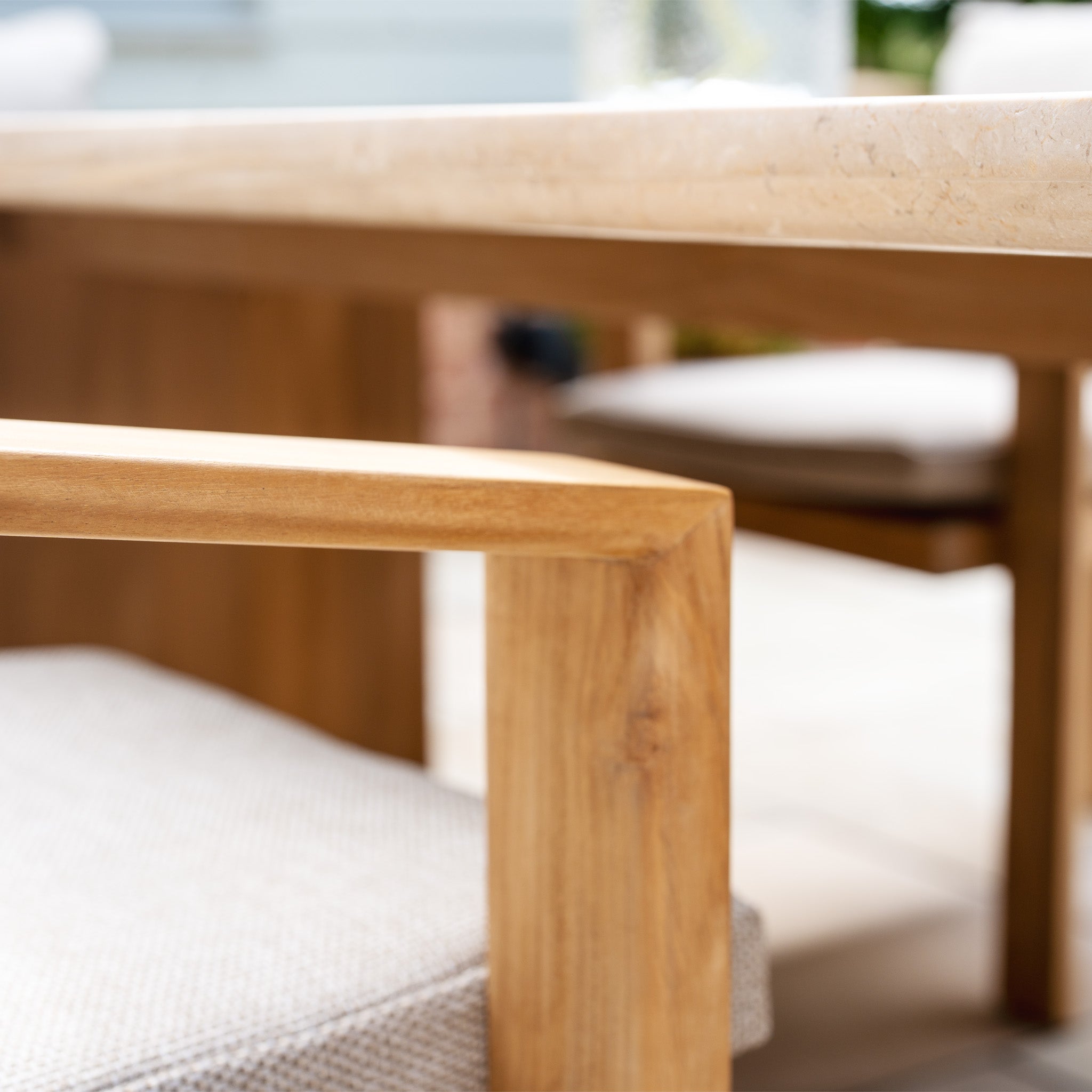 Close-up of the Tivoli 6 Seat Dining Set’s teak wood chair with beige cushion next to its Fawn marble dining table.