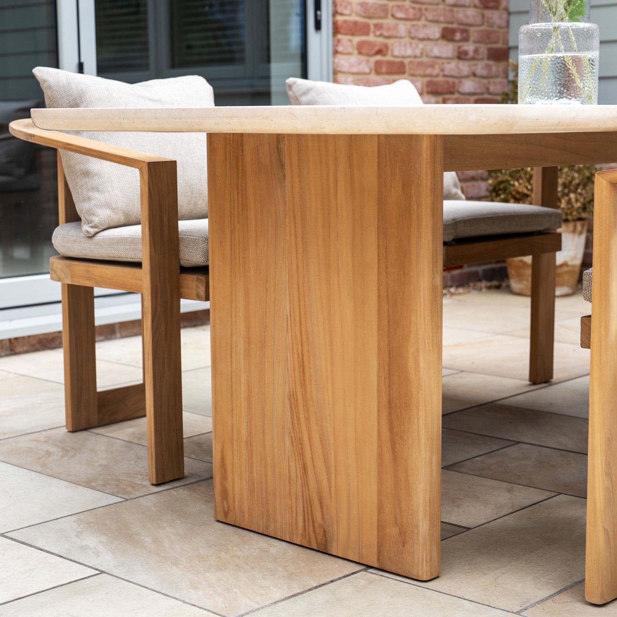 The Tivoli 6 Seat Dining Set with Marble Dining Table in Fawn features cushioned chairs arranged on a tiled patio near a glass door and brick wall.