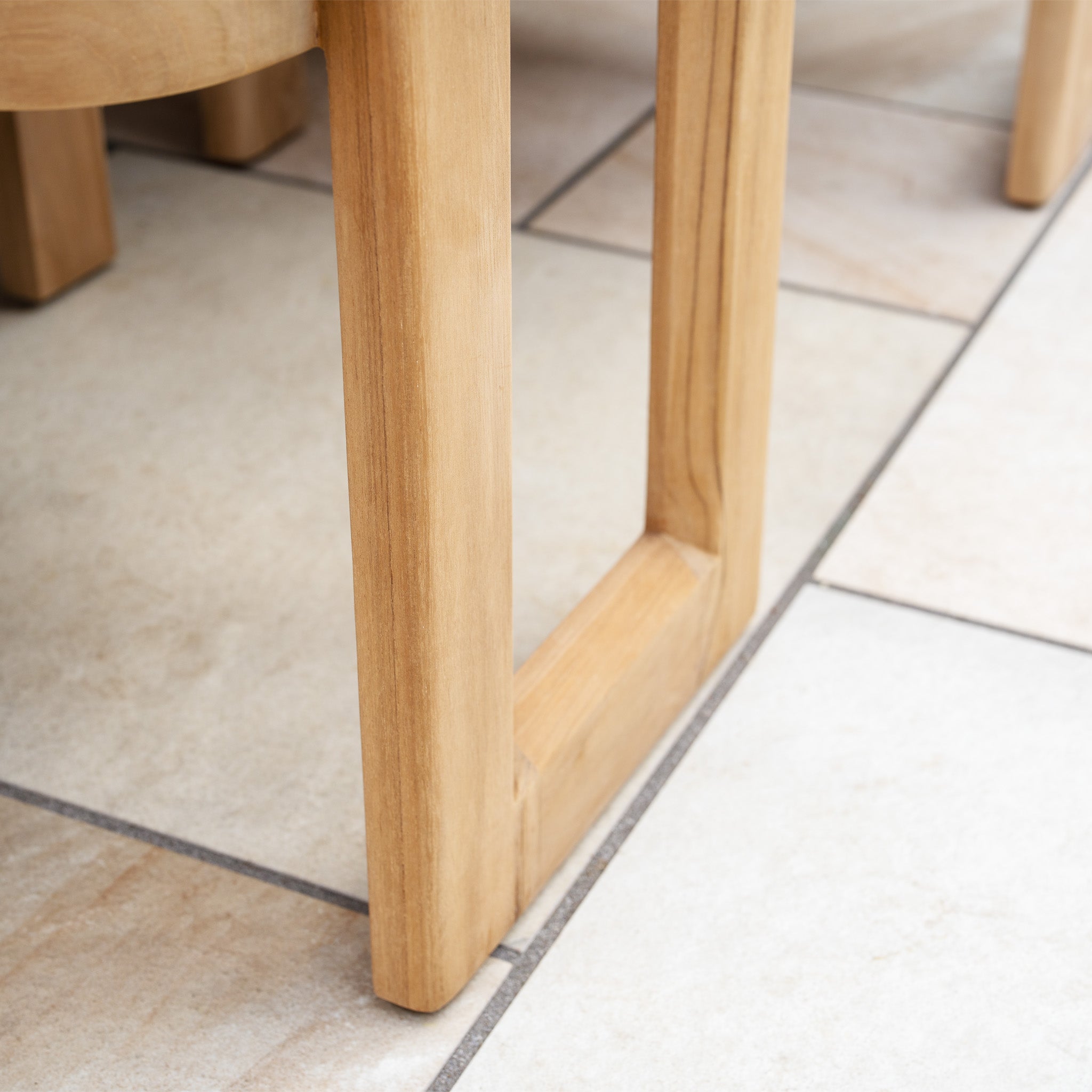 Close-up of a teak wood table or chair leg on light-colored tiled flooring, ideal for pairing with the Tivoli 6 Seat Dining Set with Marble Dining Table in Fawn.