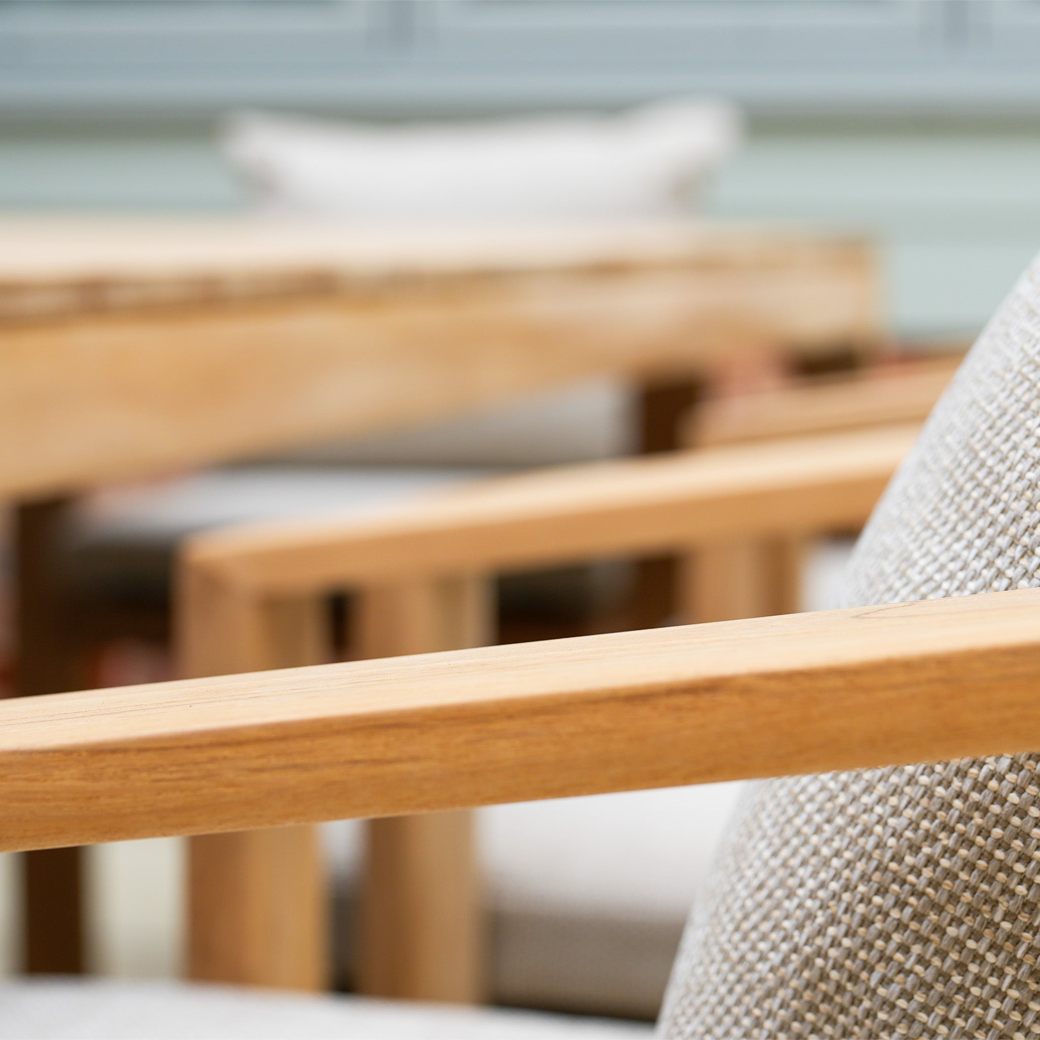 Close-up of a wooden armrest on a cushioned chair from the Tivoli 8 Seat Dining Set with Teak Dining Table in Fawn, with blurred chairs and table in the background.