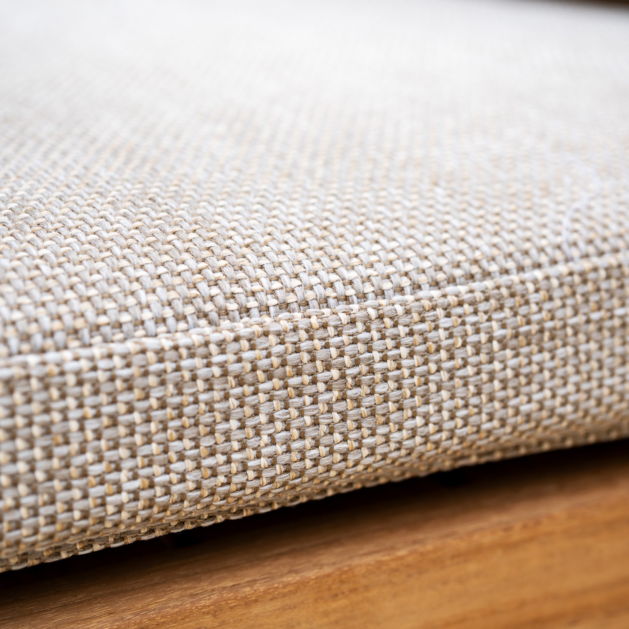 Close-up of a beige woven fabric cushion with UV resistant material, part of the Tivoli 8 Seat Dining Set with Teak Dining Table in Fawn, shown on a wooden surface.