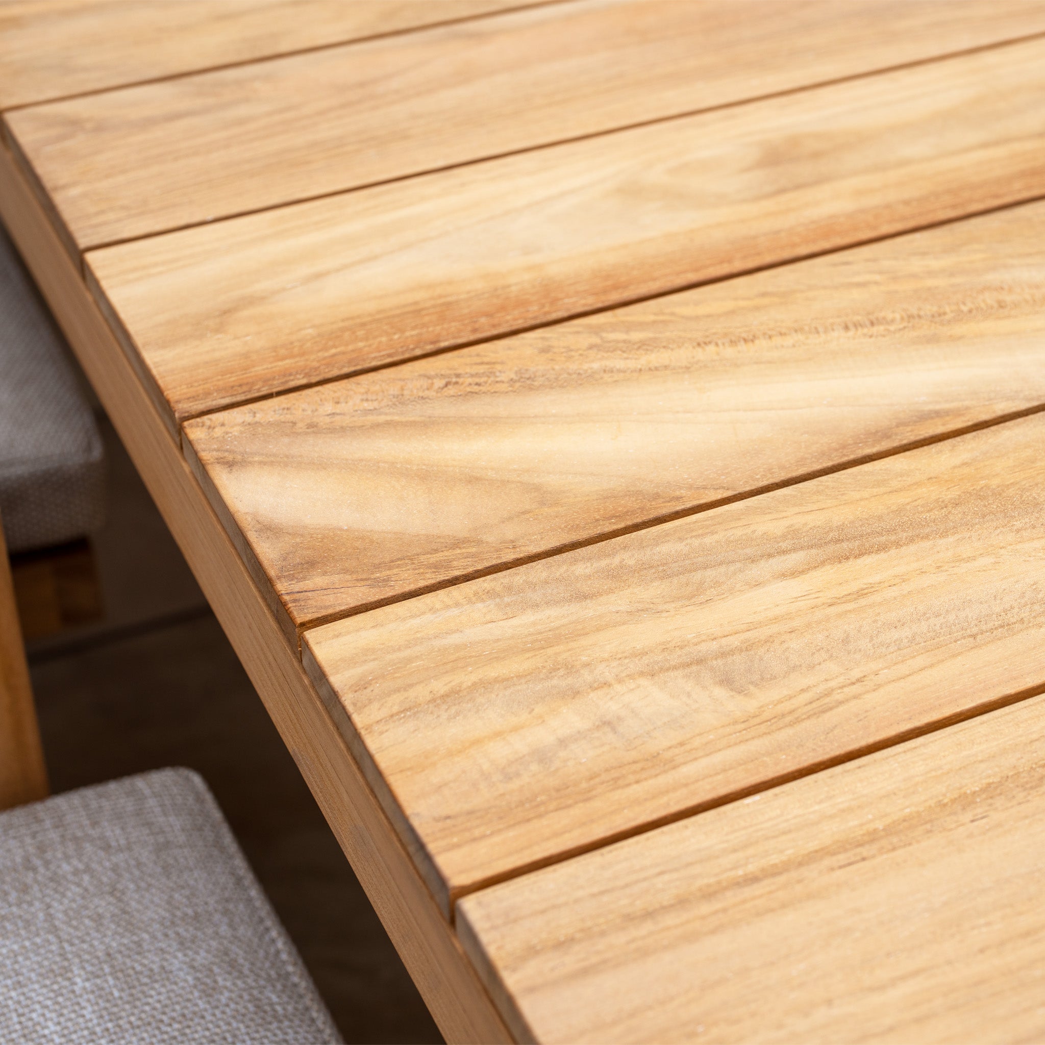 Close-up of the Tivoli 8 Seat Dining Set with Teak Dining Table in Fawn, showing its slatted tabletop and two partially visible chairs with UV resistant cushions at the sides.