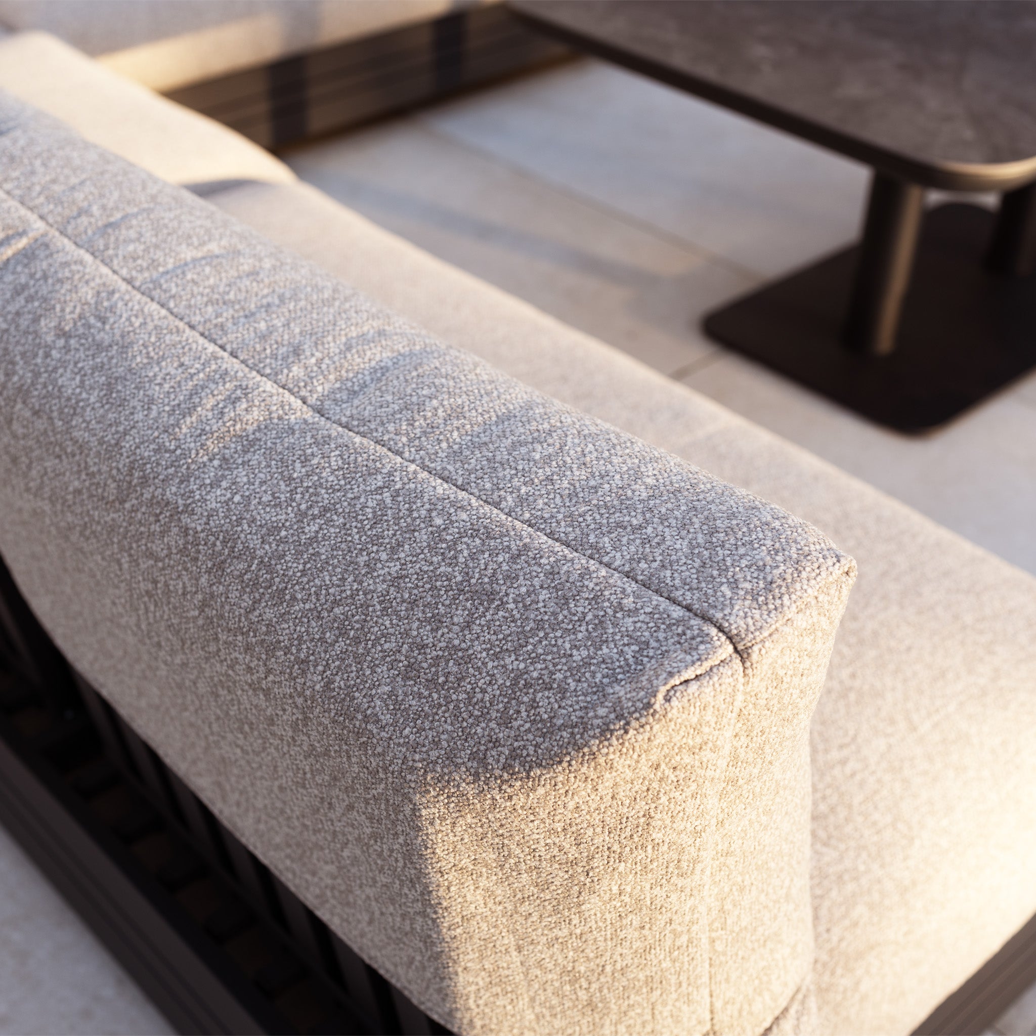 Close-up of the Savona Luxury Outdoor Large U-Shape Corner Sofa Set with Altura Rising Table in Truffle, featuring light gray upholstery and rust-proof aluminium, basking in sunlight.