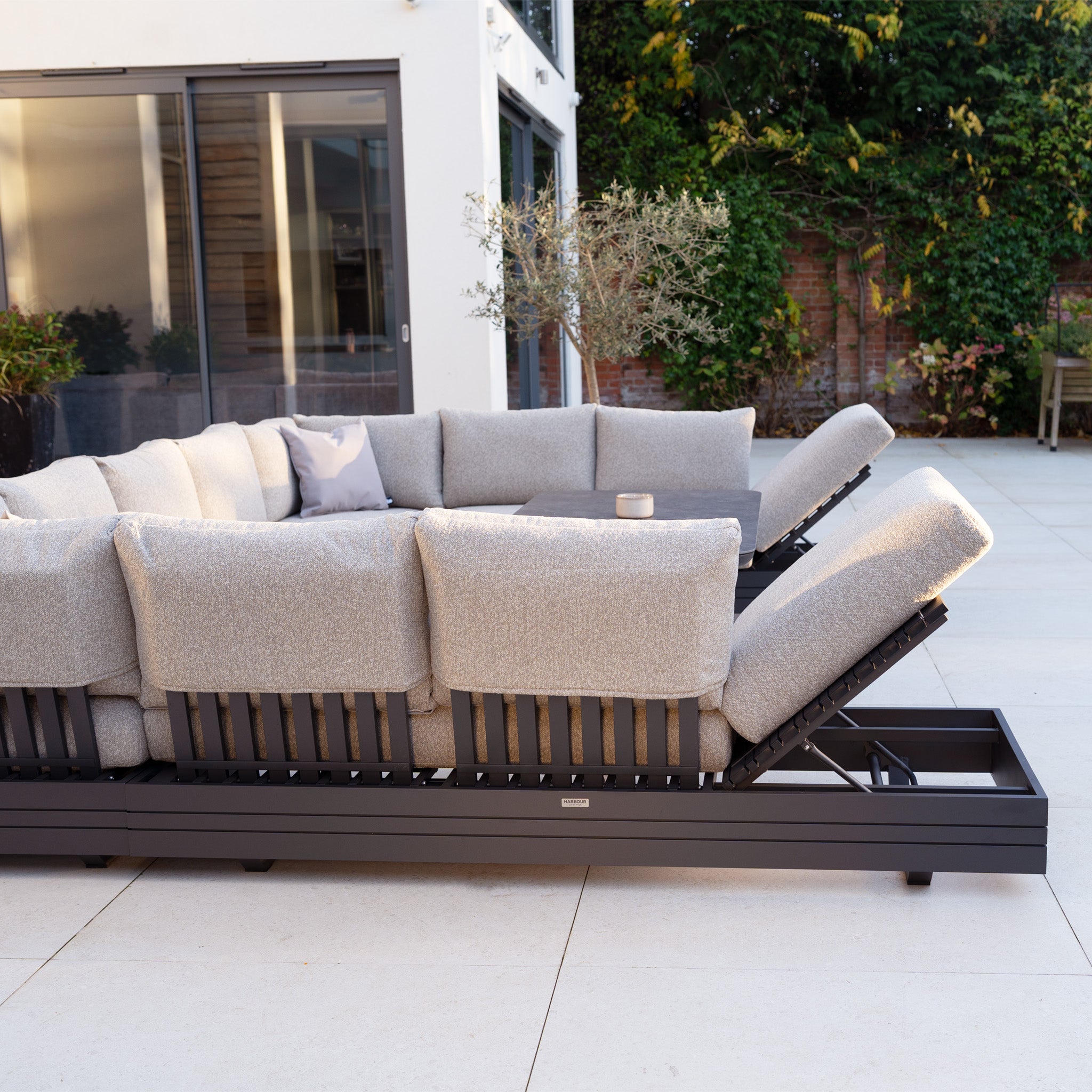 The Savona Luxury Outdoor Large U-Shape Corner Sofa Set with Altura Rising Table in Truffle features adjustable backrests and rust-proof aluminium, creating a stylish modular garden furniture arrangement for your patio or garden.
