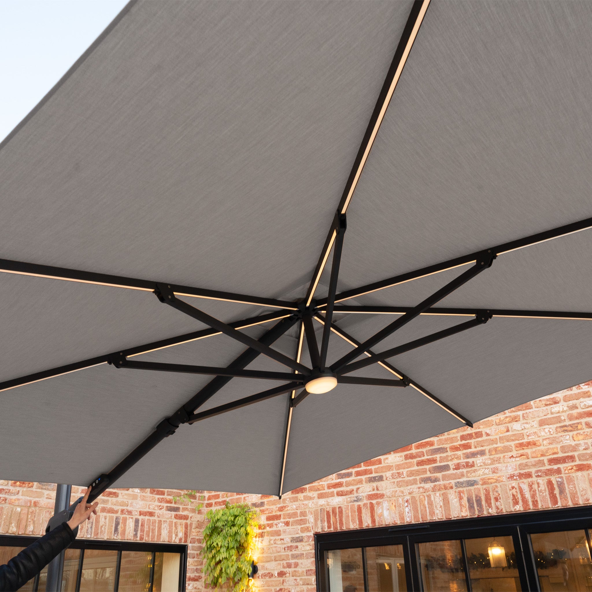 Enjoy the view from beneath the Volos 3m x 4m Rectangular Cantilever Parasol in Slate, featuring built-in LED lighting, a sturdy black frame, and a 120kg granite base—perfect for patios by brick buildings.