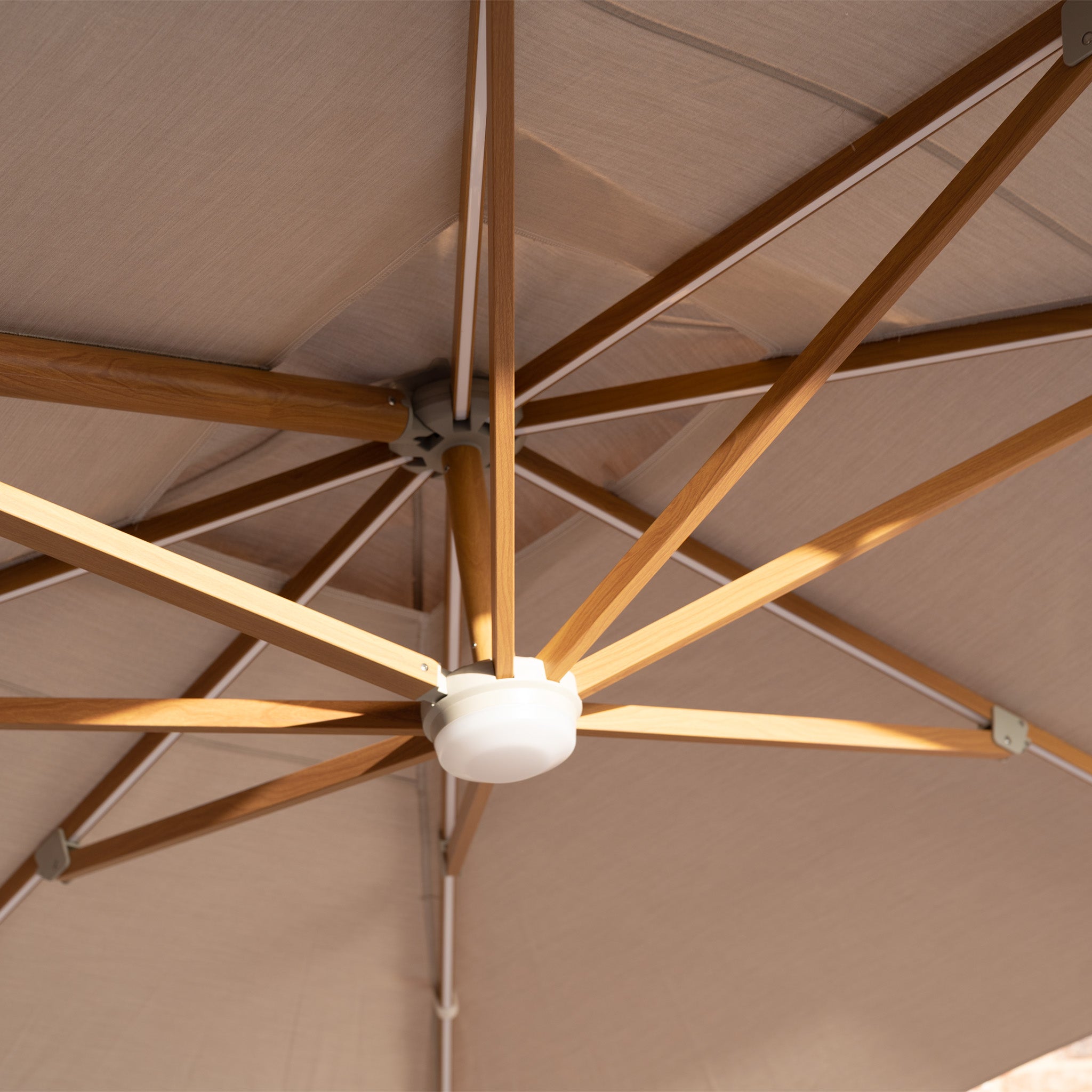 Close-up of the wood-effect frame and support structure beneath the UV-resistant Volos 3m x 3m Square Cantilever Parasol with LED lighting and a 120kg granite base, highlighting its sturdy wheat-colored design.