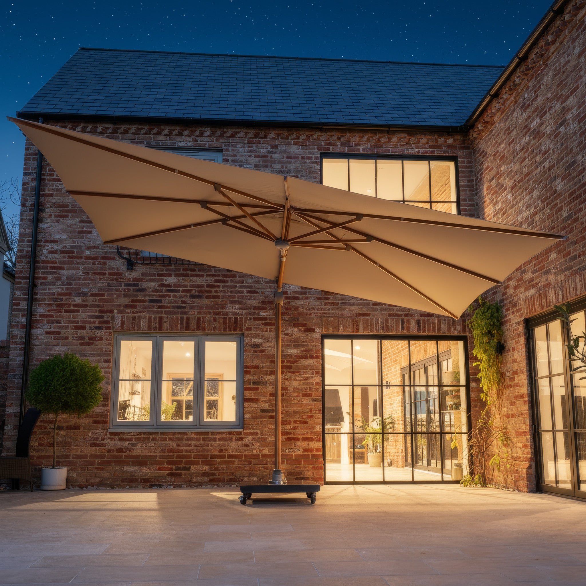 The Volos 3m x 4m Rectangular Cantilever Parasol in Wheat and Wood Effect, with a UV-resistant canopy, LED lighting, and a 120kg granite base, stands illuminated in a brick house courtyard at night.