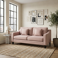 Wiltshire 2 Seat Sofa in Dusky Pink with cushions, styled in a modern living room featuring wall art, large windows, and a potted plant.