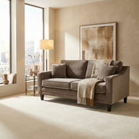 A modern living room featuring the Wiltshire 2 Seat Velvet Sofa in Mink, a cozy throw blanket, a stylish lamp, abstract art, and large windows overlooking city views.