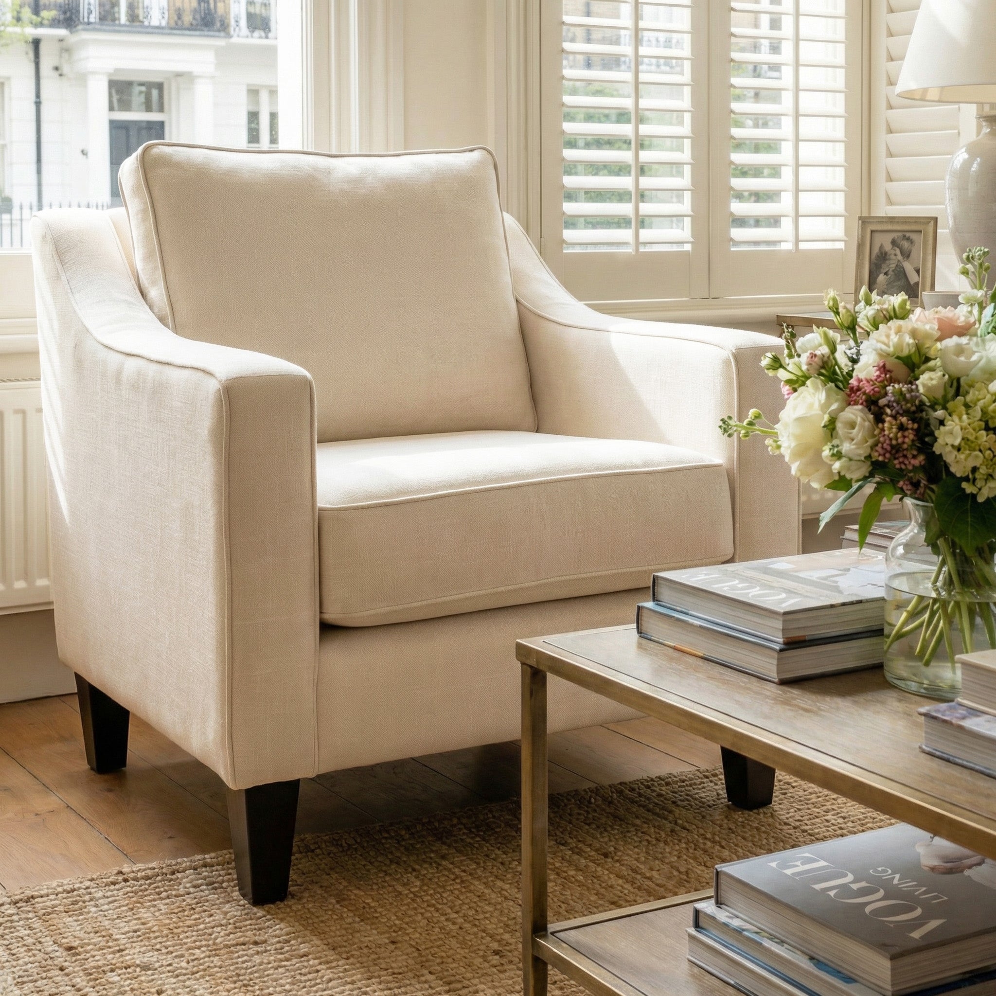 Wiltshire Armchair in Ivory beside a coffee table with books and flowers in a bright, sunlit living room.