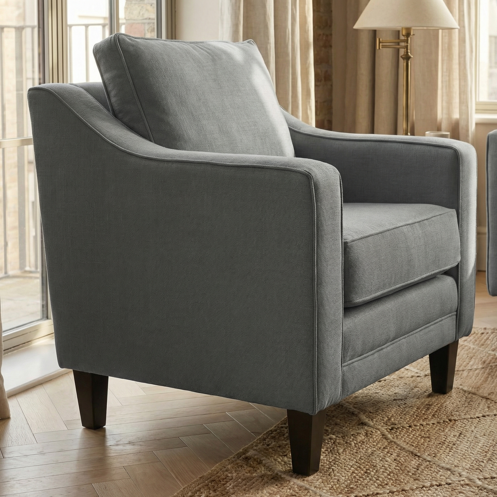 The Wiltshire Armchair in Smoke Grey with dark wooden legs sits on a woven rug near large windows and beige curtains.